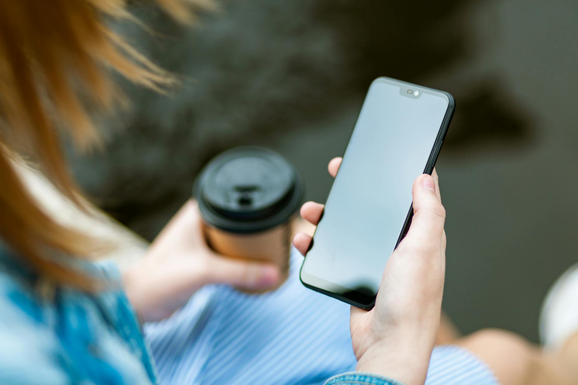 Une femme tenant son téléphone et un gobelet à café | Source : Pexels