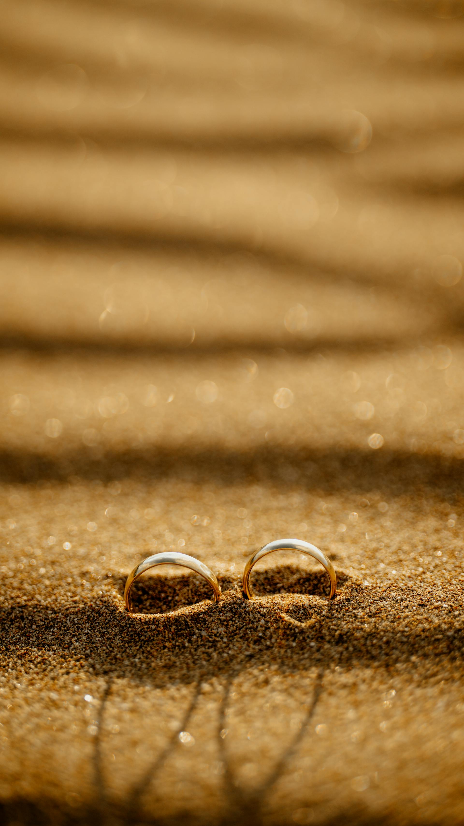 Des anneaux de mariage sur une plage de sable au coucher du soleil | Source : Pexels