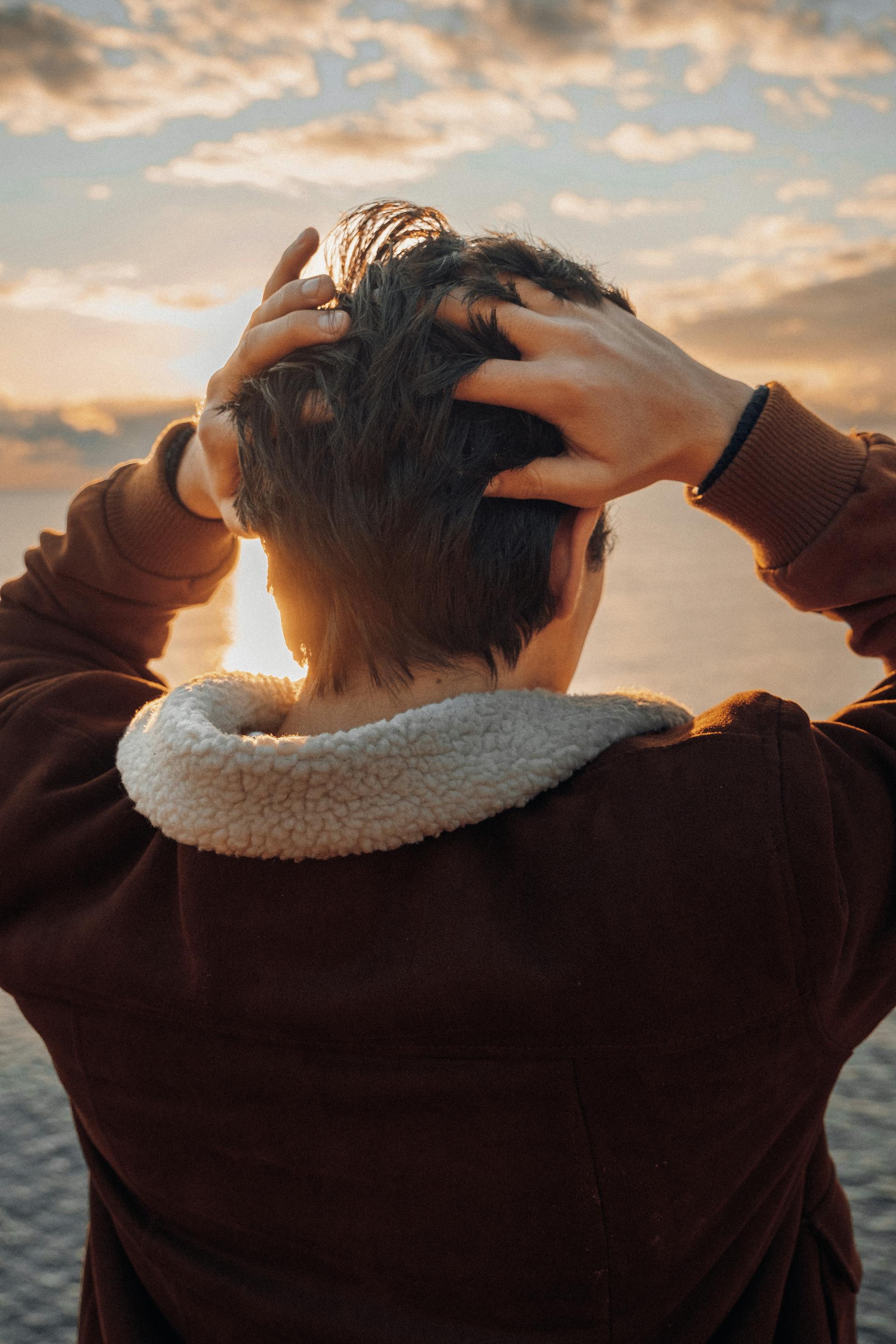 Un jeune se touche l'arrière de la tête alors qu'il se trouve sur la plage | Source : Pexels