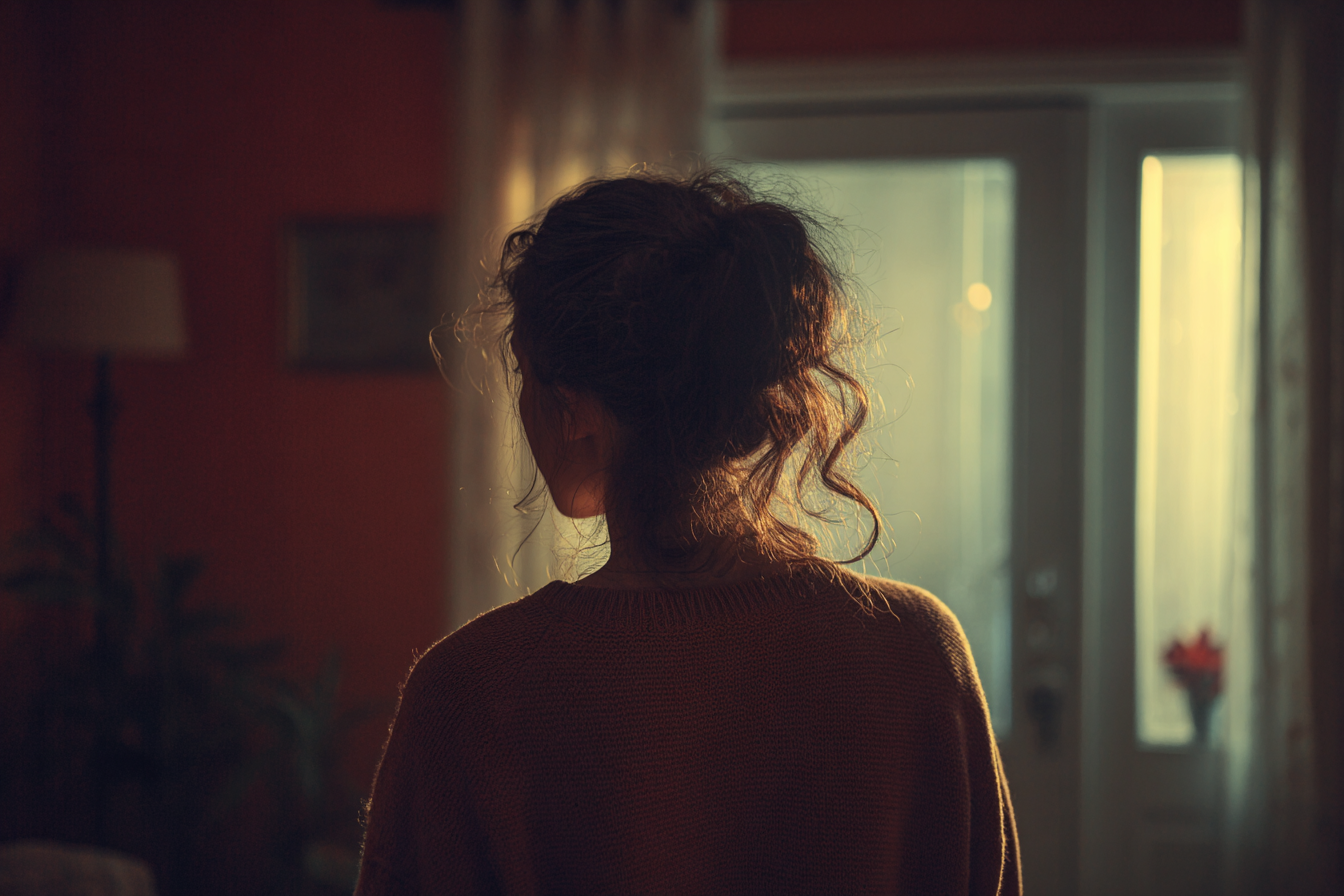 Une jeune femme debout près d'une fenêtre | Source : Midjourney