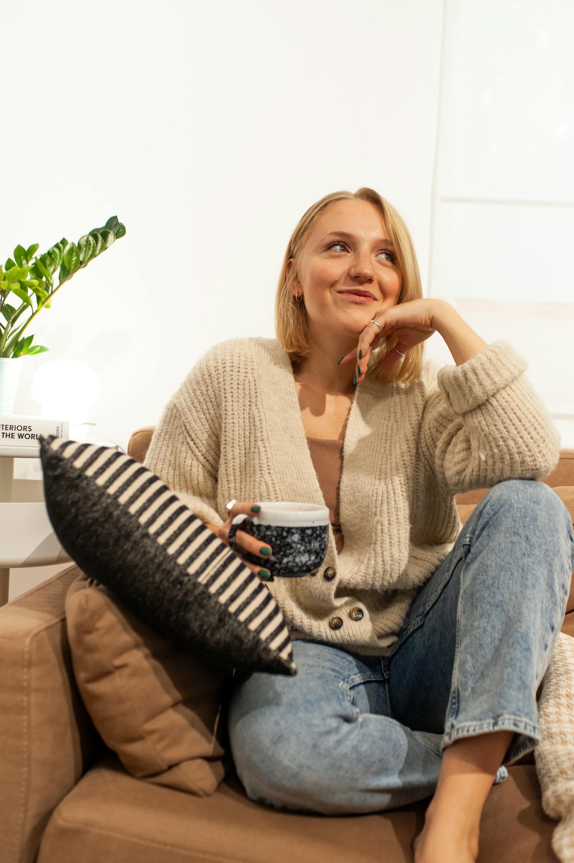 Une femme souriante assise sur un canapé tout en tenant une tasse de café | Source : Pexels