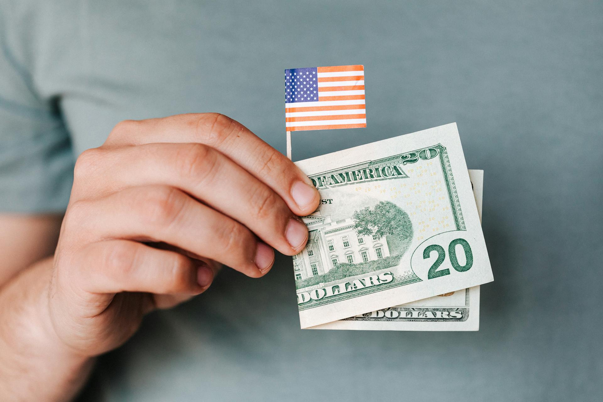 Un homme tenant un billet de 20 dollars et un drapeau américain miniature | Source : Pexels