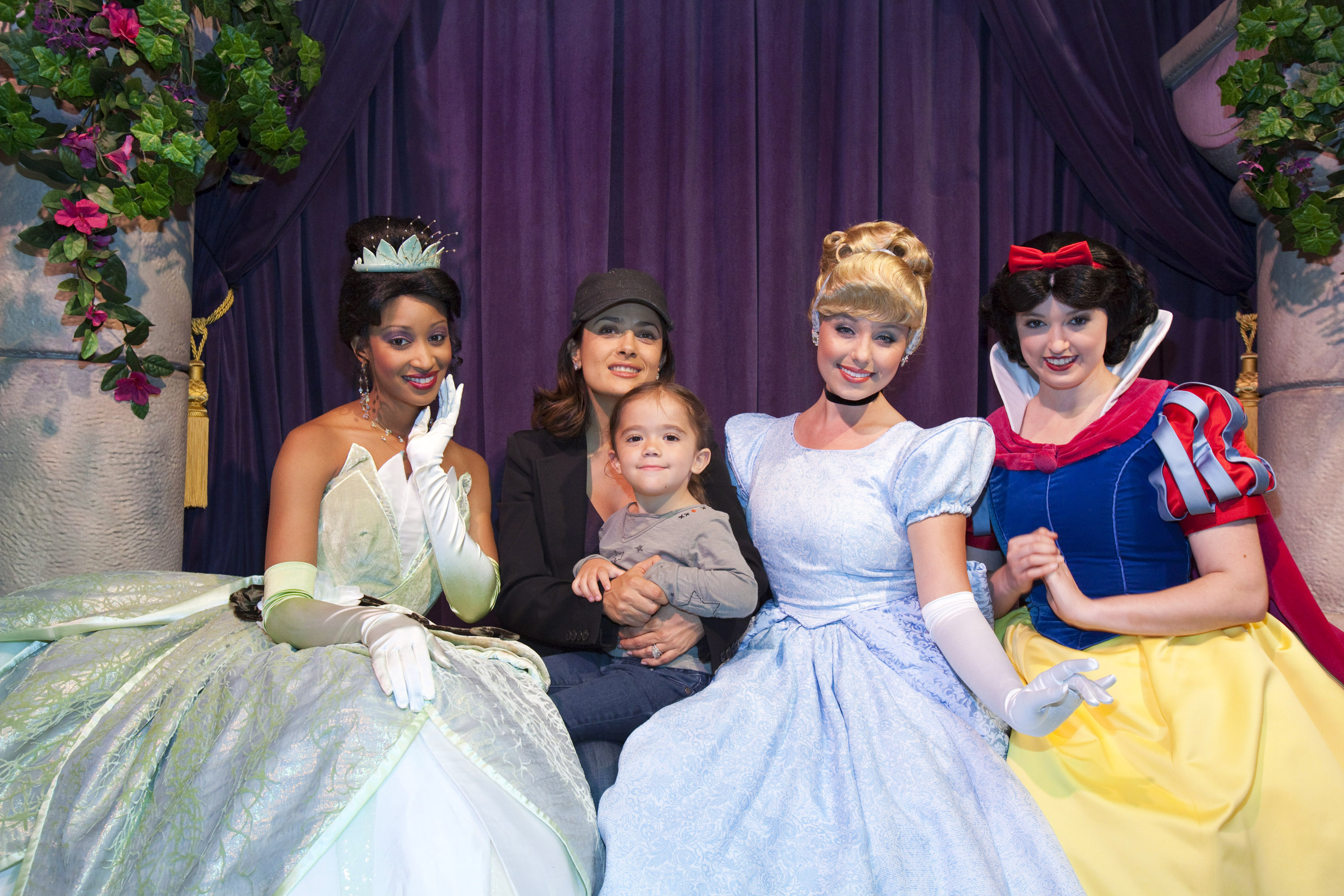 Lors d'une charmante sortie en famille à Disneyland, Salma Hayek et Valentina Pinault posent aux côtés des princesses Disney emblématiques Tiana, Cendrillon et Blanche-Neige. Salma, vêtue d'une casquette et d'une veste noires, rayonne de bonheur en serrant sa fille dans ses bras. Valentina, confortablement installée sur les genoux de sa mère, porte un haut gris et un jean, et son expression mêle admiration et joie tranquille.