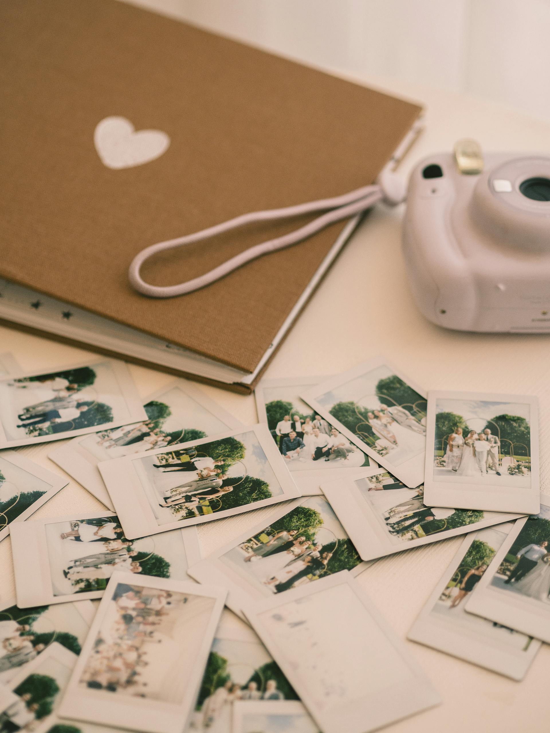 Un appareil photo, un album photo et des photos posés sur une surface blanche | Source : Pexels