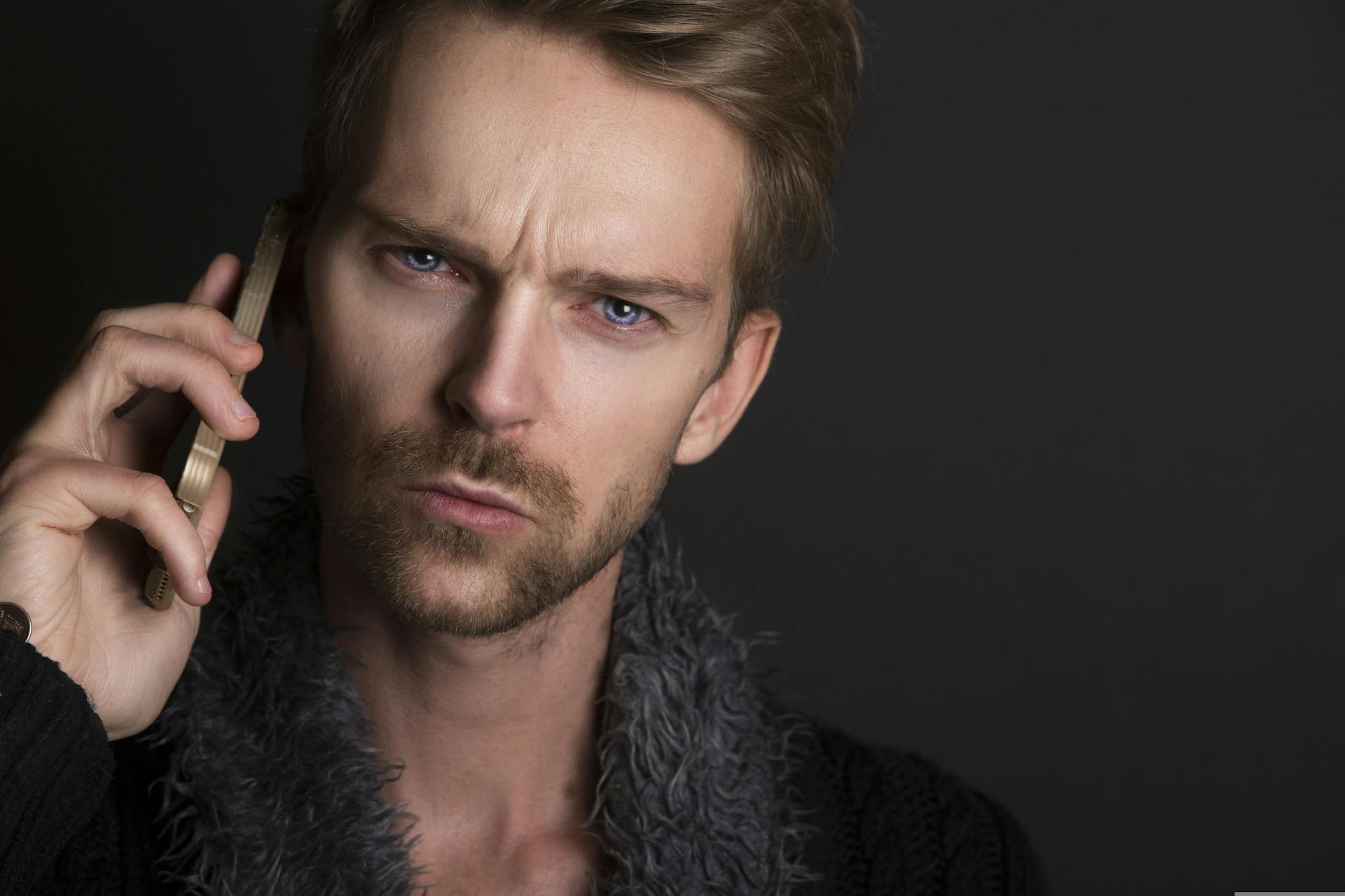 Un homme aux yeux bleus et au sourcil froncé parlant au téléphone | Source : Pexels