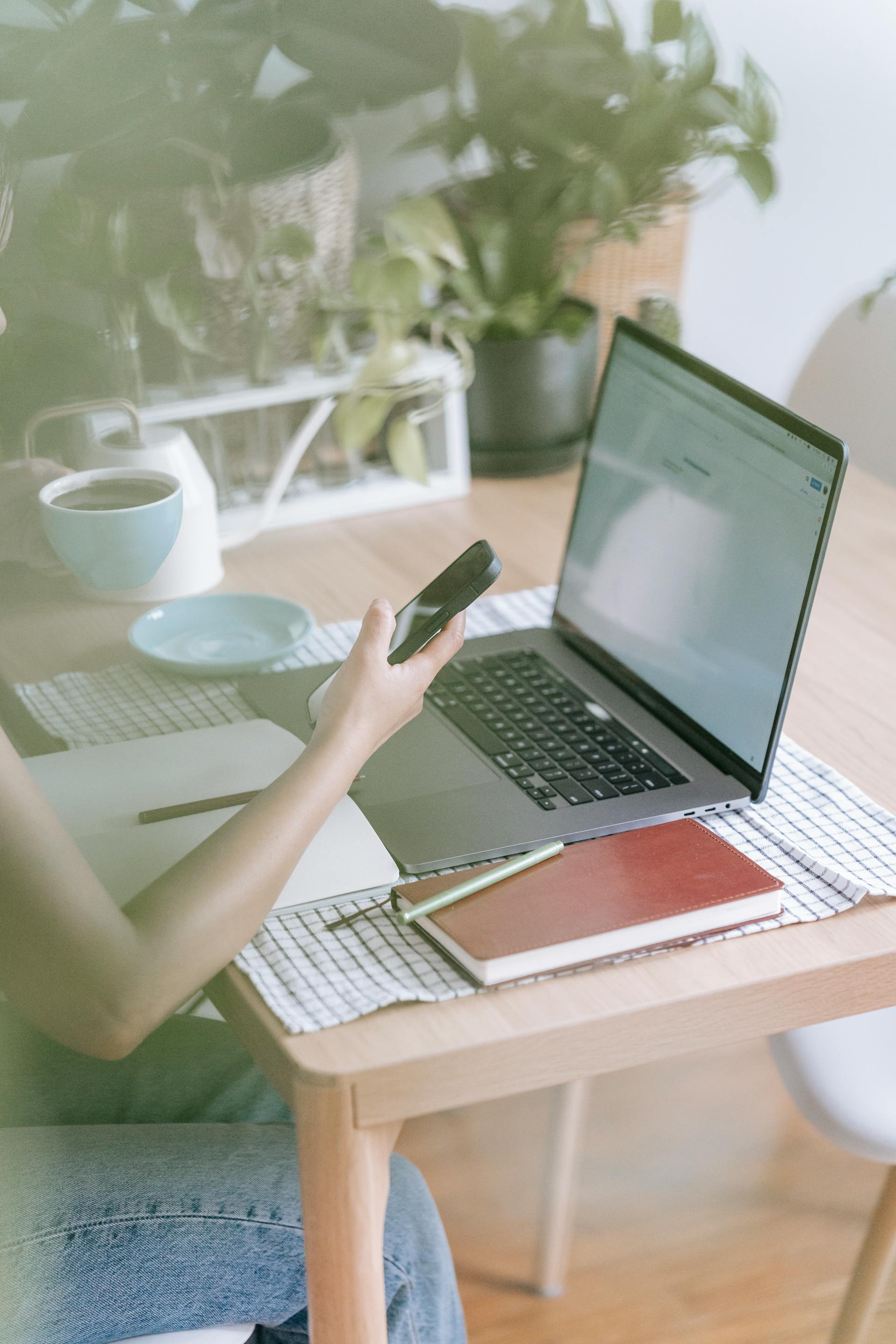 Gros plan sur une femme qui tient son téléphone tout en travaillant sur son ordinateur portable | Source : Pexels