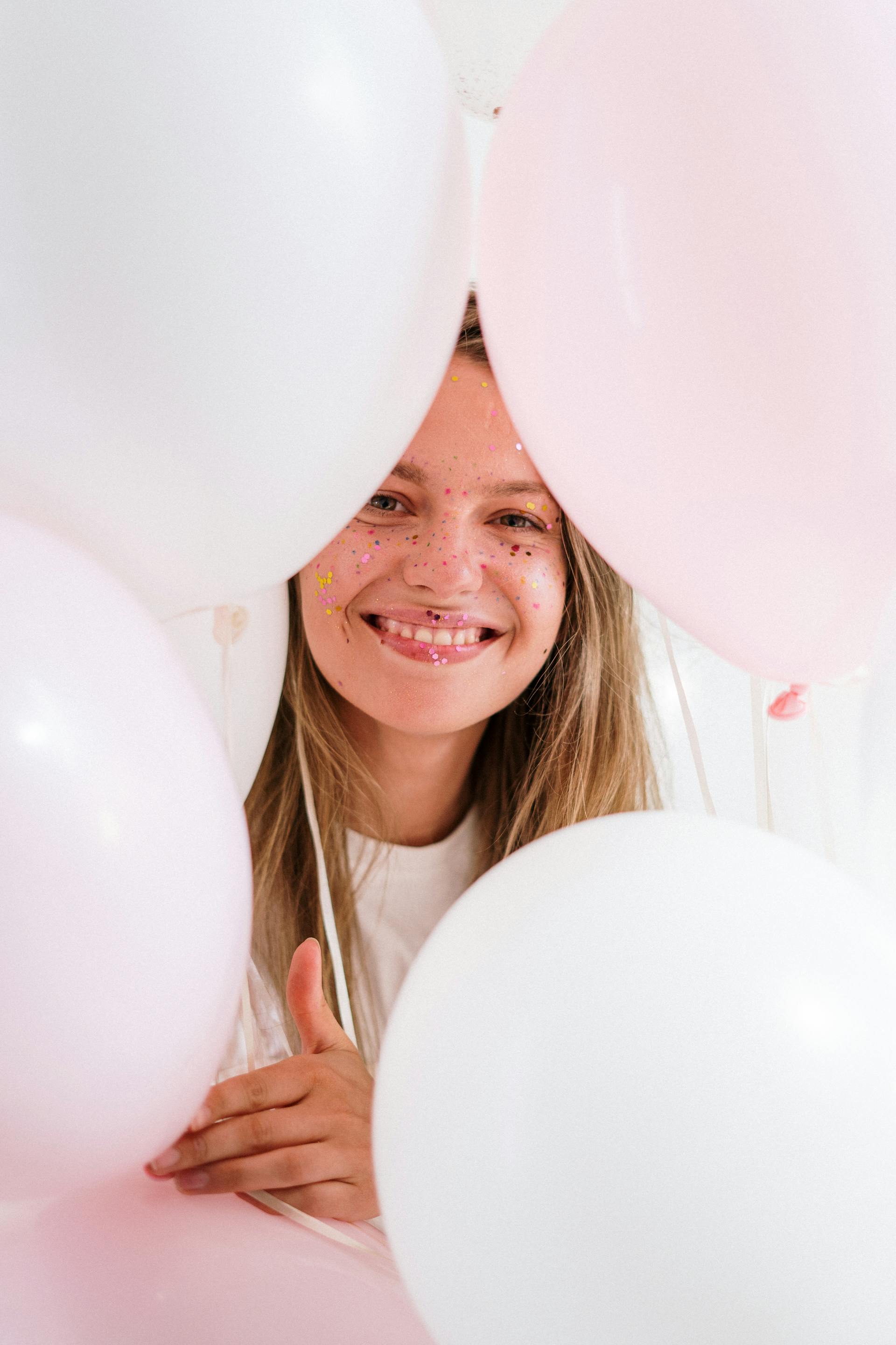 Une jeune fille souriante tenant des ballons roses et blancs | Source : Pexels