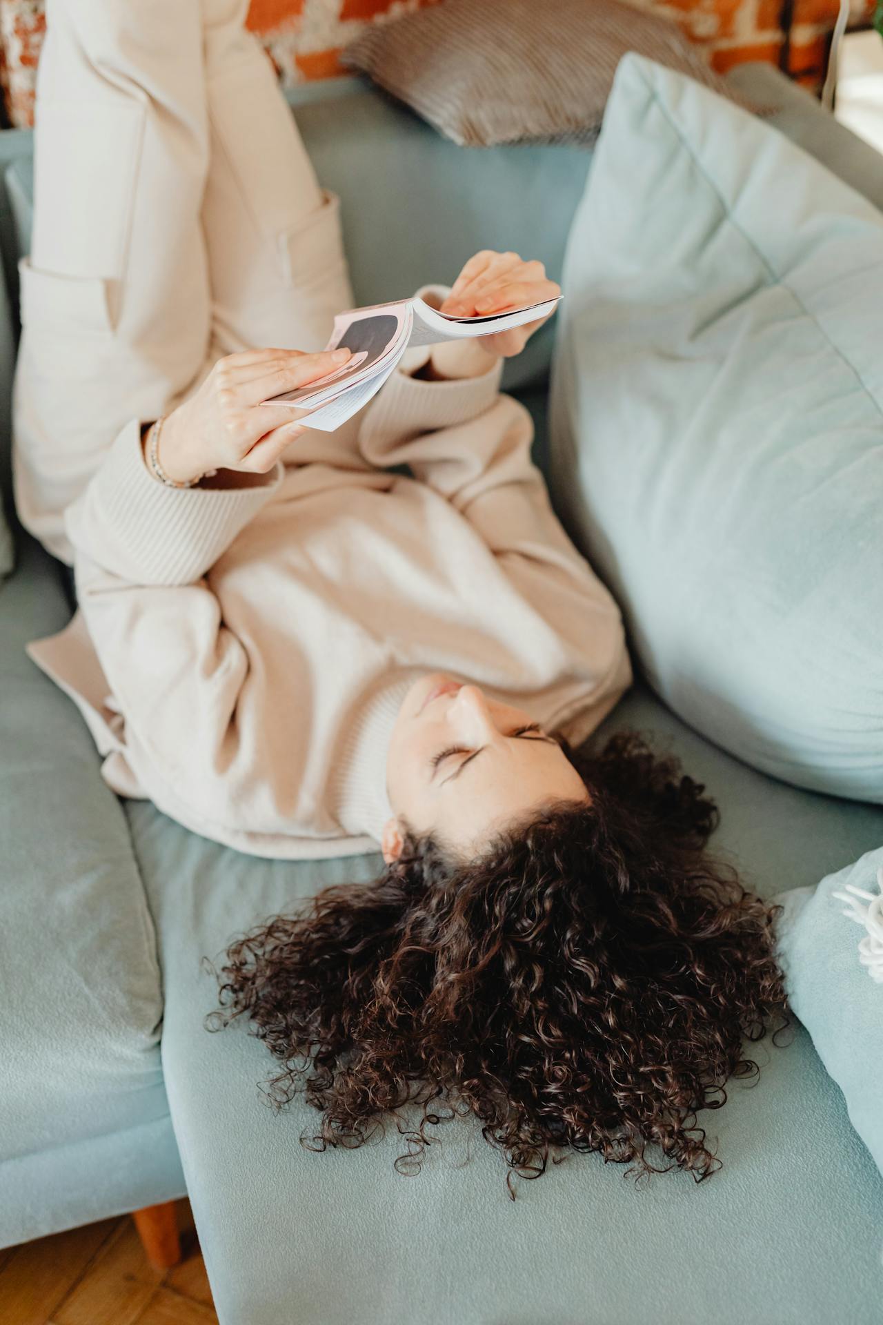 Une femme allongée sur le canapé et lisant un livre | Source : Pexels