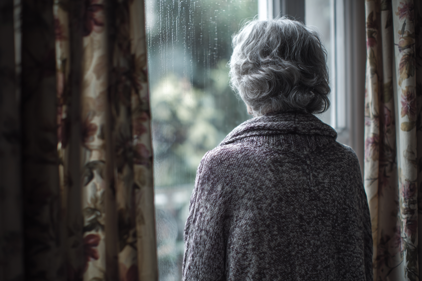 Une femme âgée debout près d'une fenêtre | Source : Midjourney