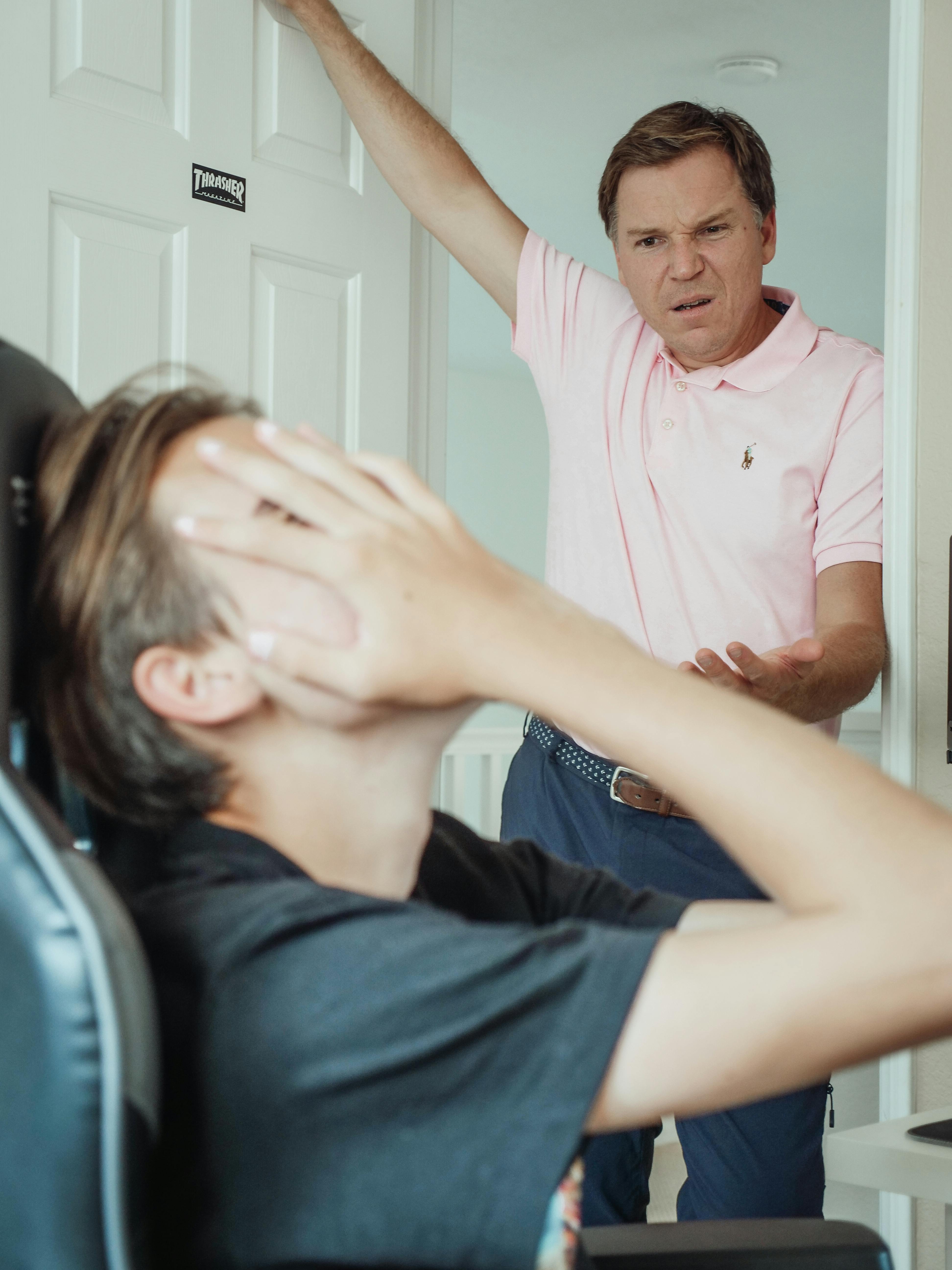 Un fils irrité se couvrant le visage pendant que son père lui parle | Source : Pexels