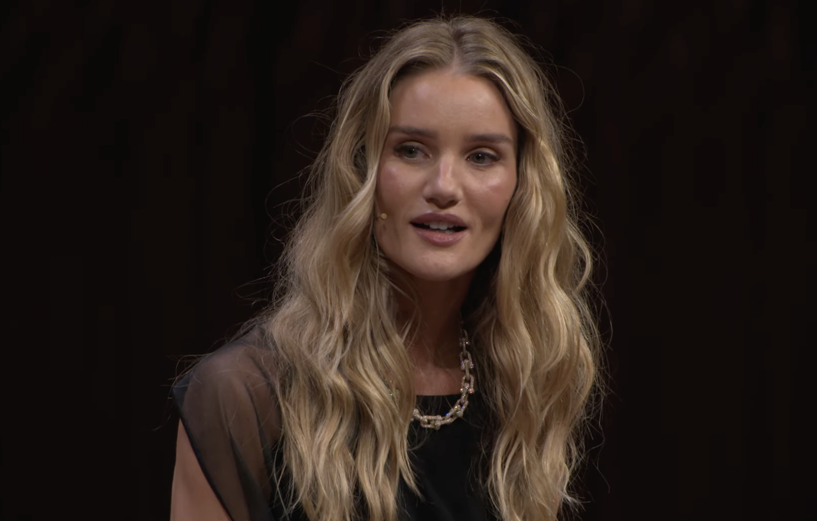 Rosie Huntington-Whiteley se retourne légèrement au milieu d'une conversation sur scène, ses cheveux blonds lâchés encadrant son visage alors qu'elle parle dans un micro-casque discret. | Source : YouTube/VogueAustralia