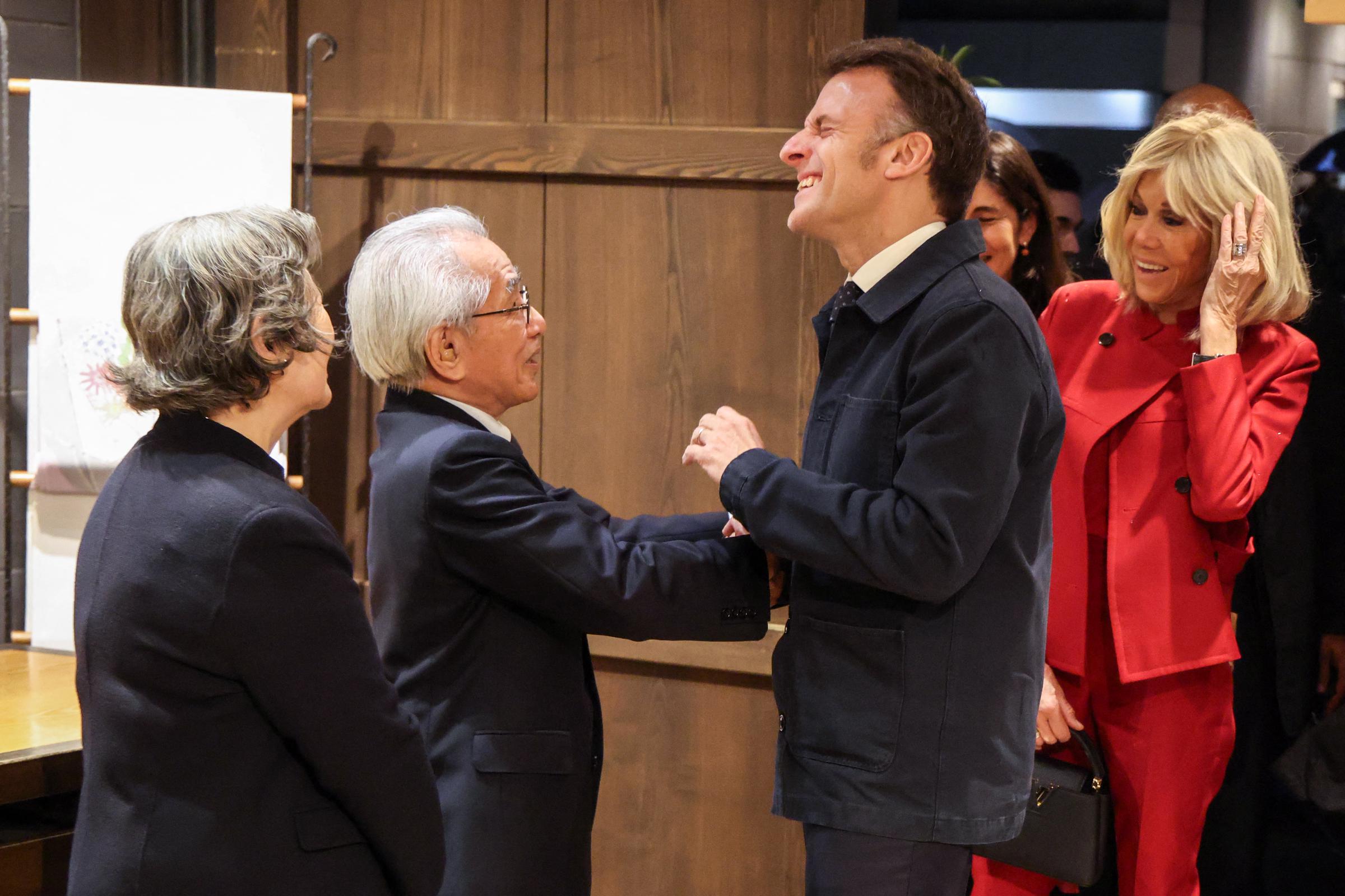 Le président français Emmanuel Macron (2e à droite) et son épouse Brigitte Macron (à droite) sont accueillis par l'artiste textile japonais Kunihiko Moriguchi (2e à gauche) au showroom Ginza Motoji à Tokyo, le 31 mars 2026 I Source : Getty Images