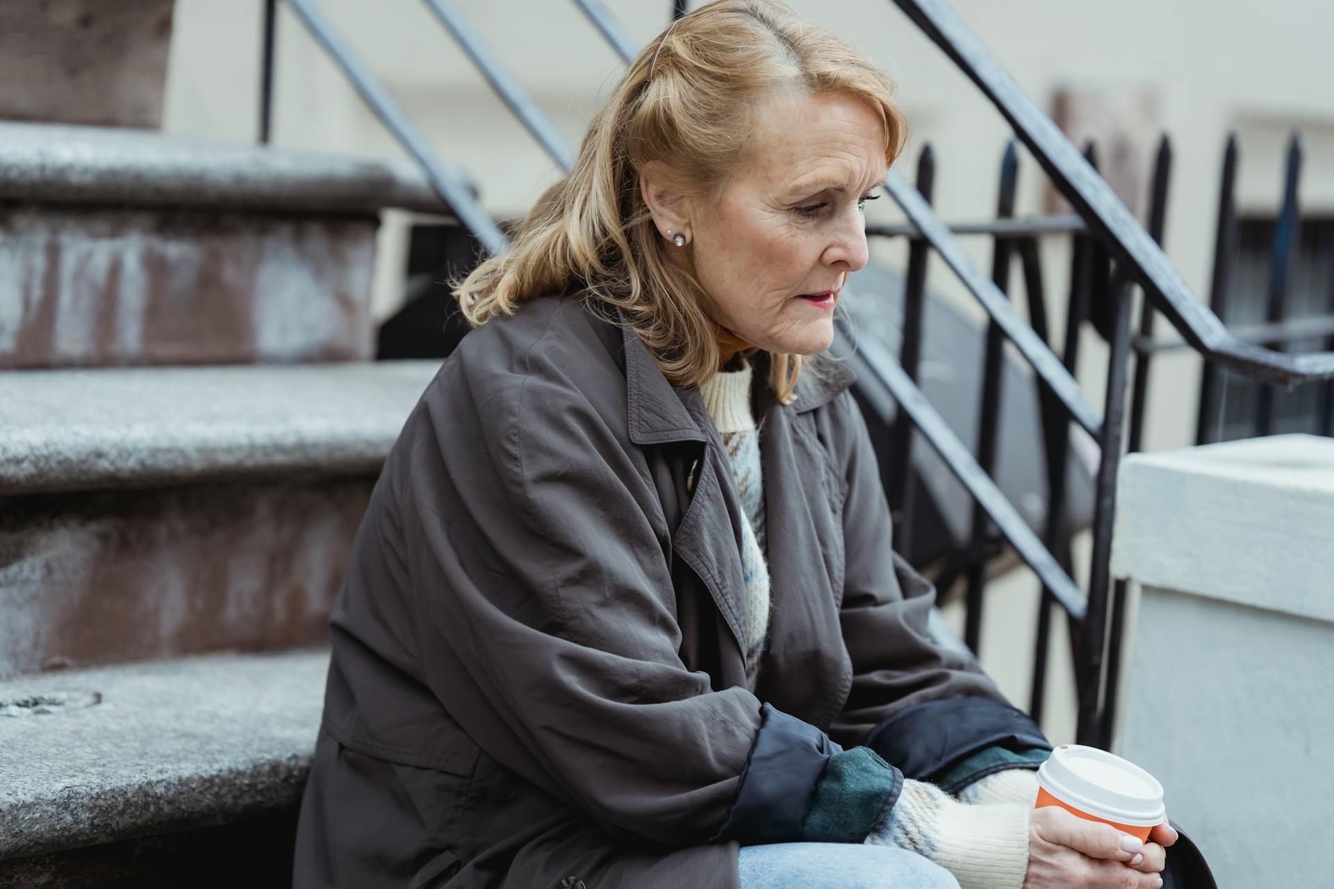 Une femme triste tenant un café à emporter, assise sur un escalier | Source : Pexels