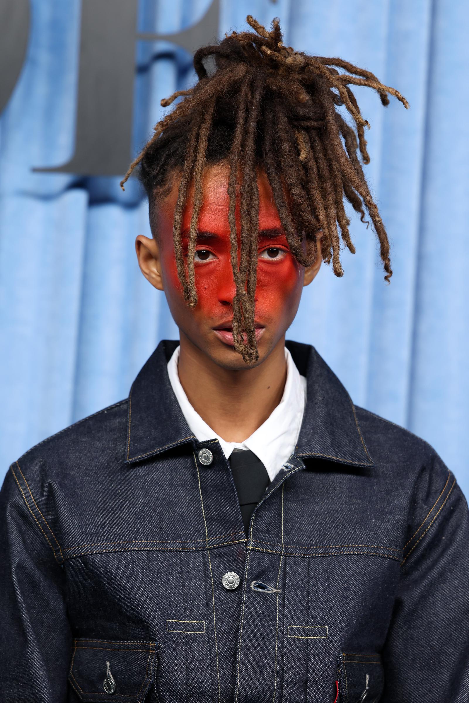 Jaden Smith participe au gala BoF500 pendant la Fashion Week de Paris, en France. Ses dreadlocks brunes mi-longues, associées à une coupe rasée sur les côtés, sont relevées en chignon, et il arbore un maquillage original qui fait ressortir le rouge au centre de son visage. Sur ce gros plan, il regarde droit devant lui dans une pose saisissante, digne d'un mannequin.