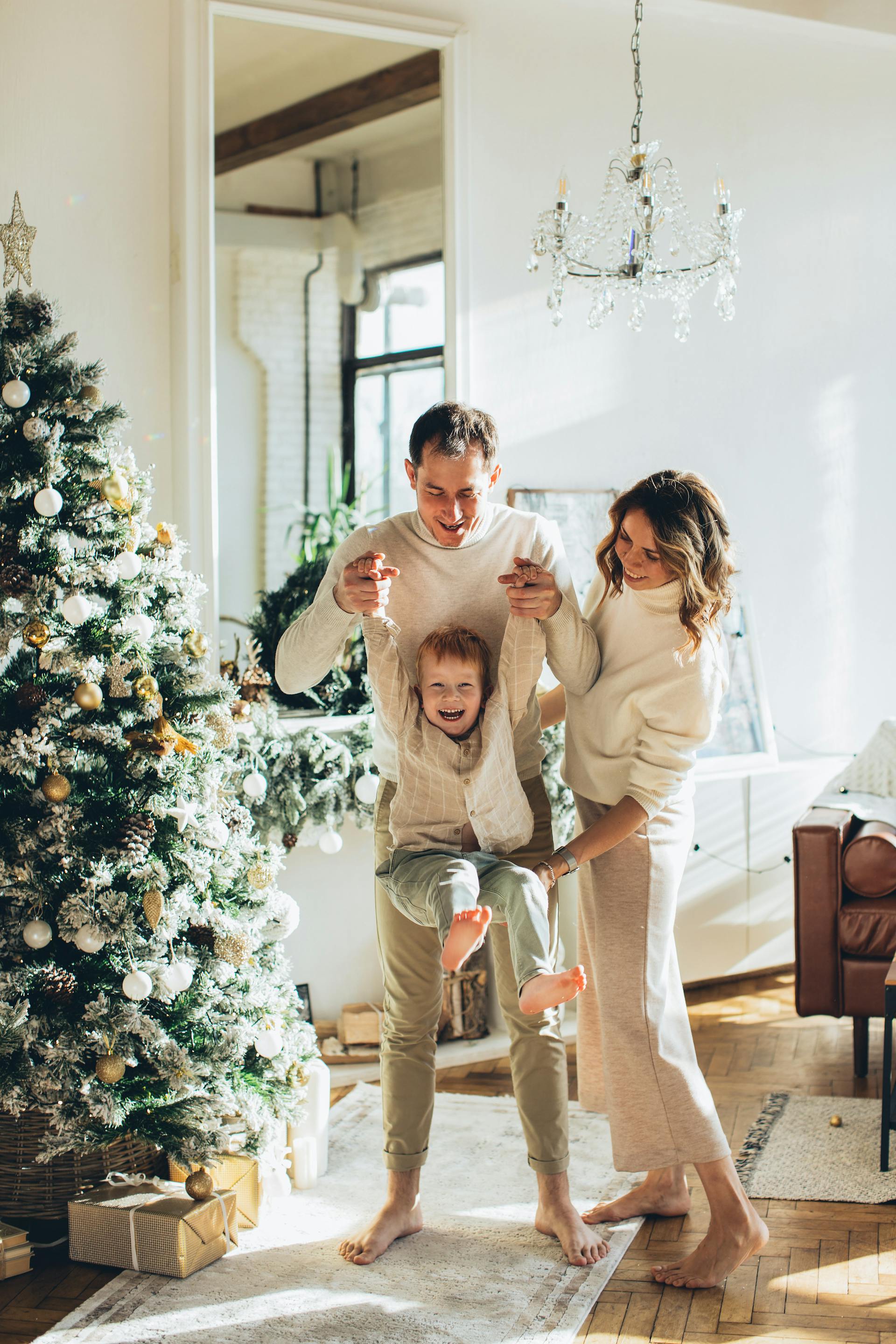 Un couple jouant avec son jeune fils à côté d'un sapin de Noël | Source : Pexels