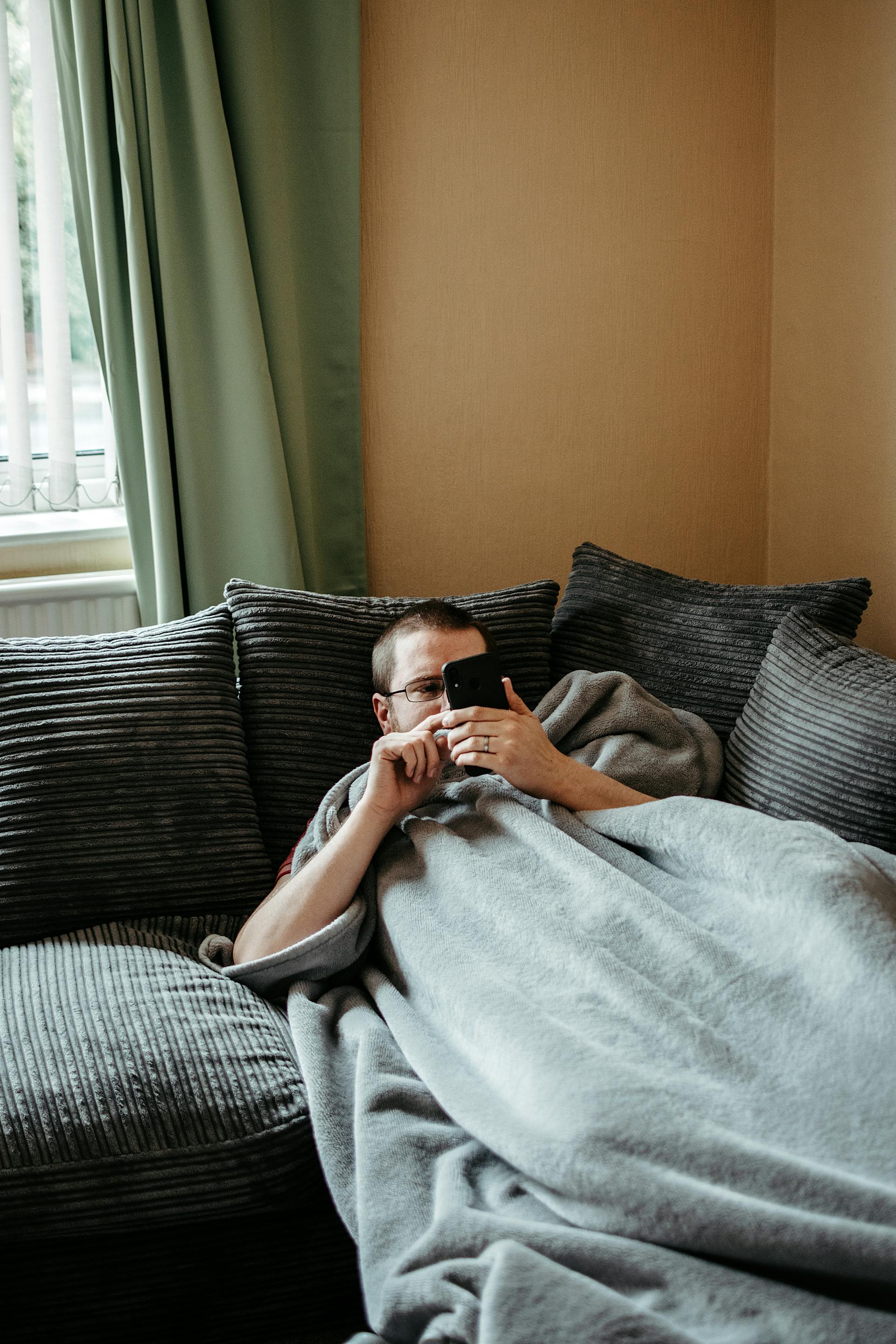 Un homme utilisant son téléphone alors qu'il est allongé sur le canapé | Source : Pexels