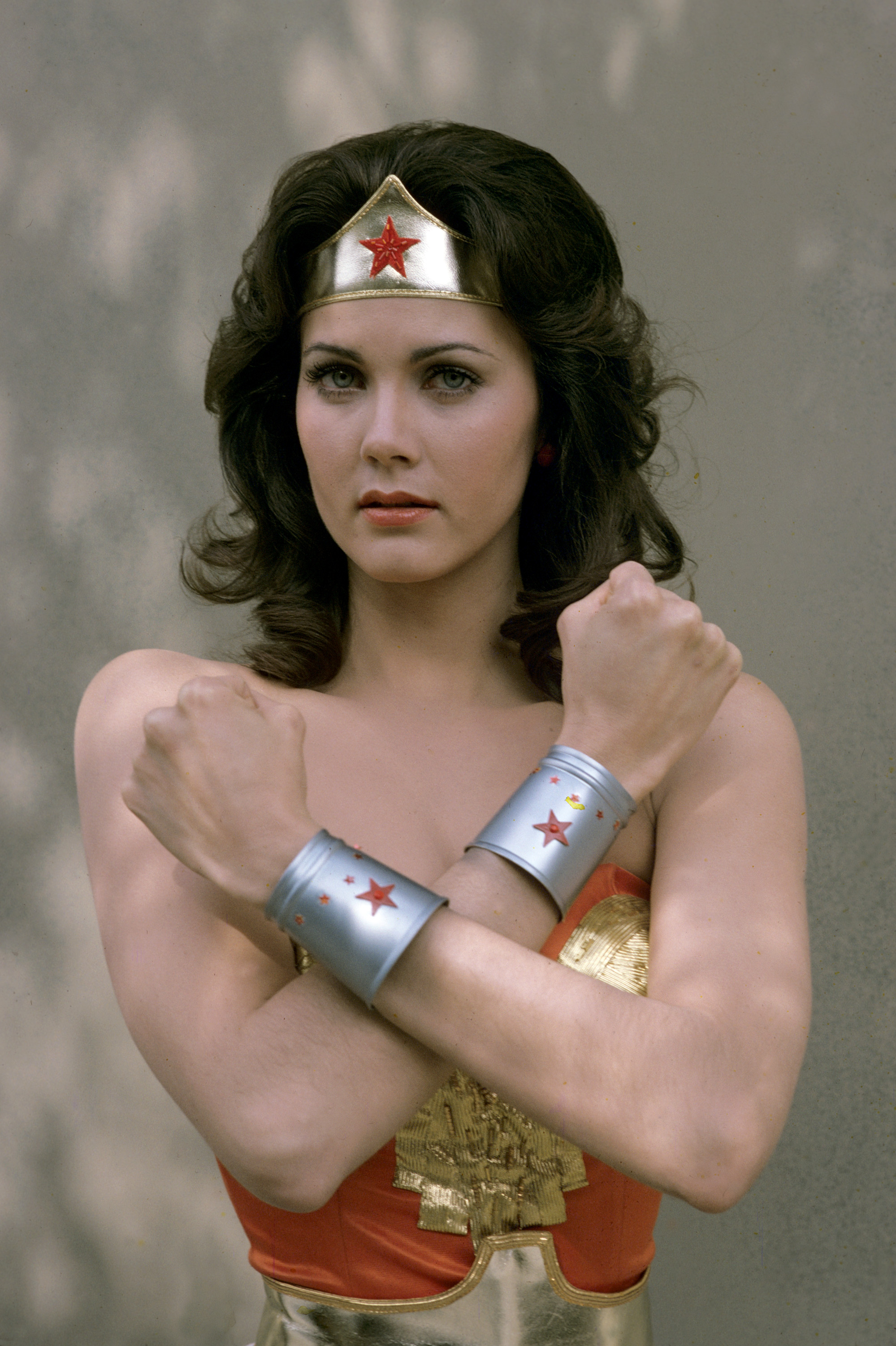 Lynda Carter, vêtue du costume complet de « Wonder Woman », prend la pose emblématique lors d'une séance photo promotionnelle pour la série télévisée. Portant sa tiare dorée caractéristique et ses bracelets argentés ornés d'étoiles rouges, elle regarde l'objectif avec une intensité tranquille.