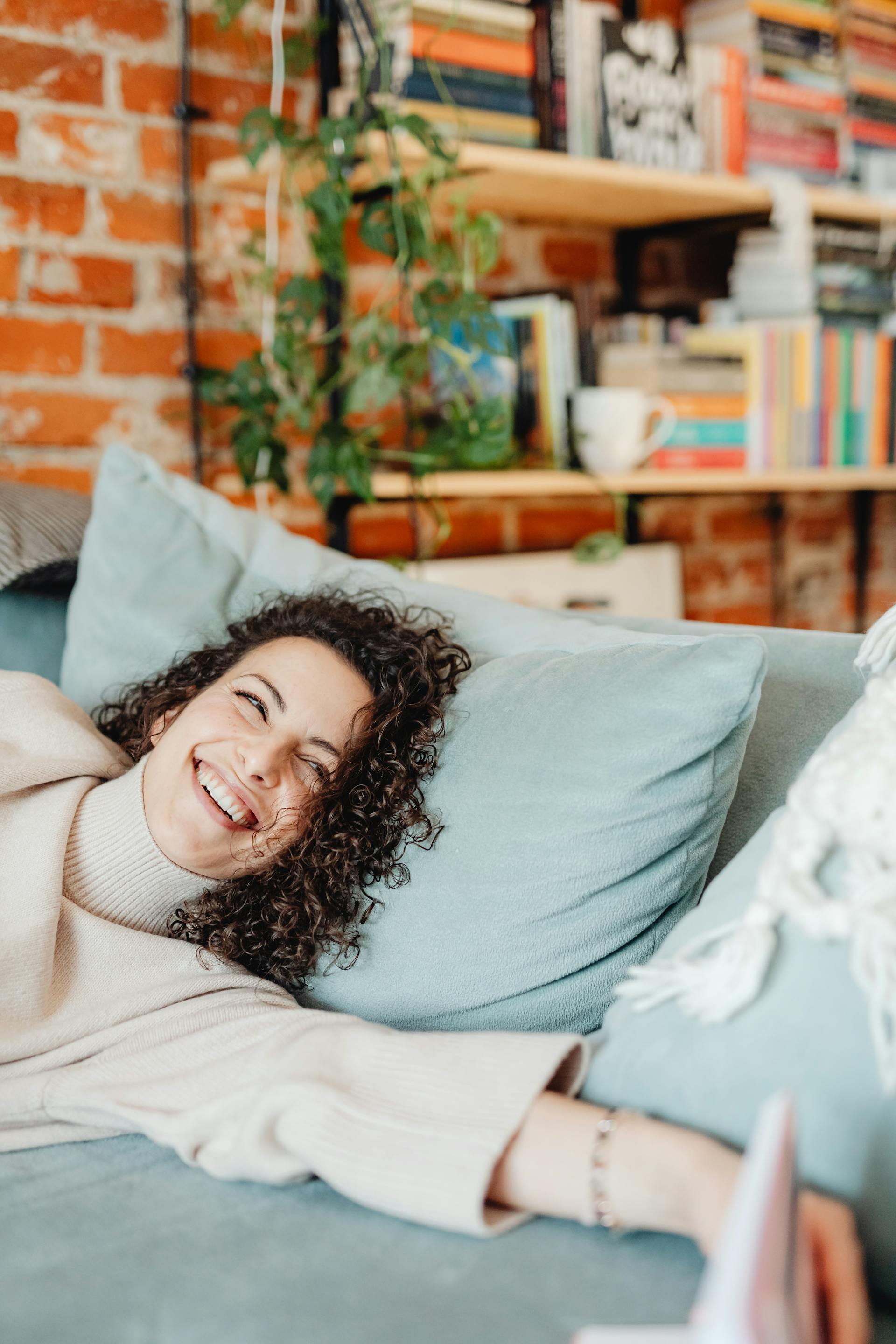 Une femme heureuse allongée sur un canapé, le sourire aux lèvres | Source : Pexels
