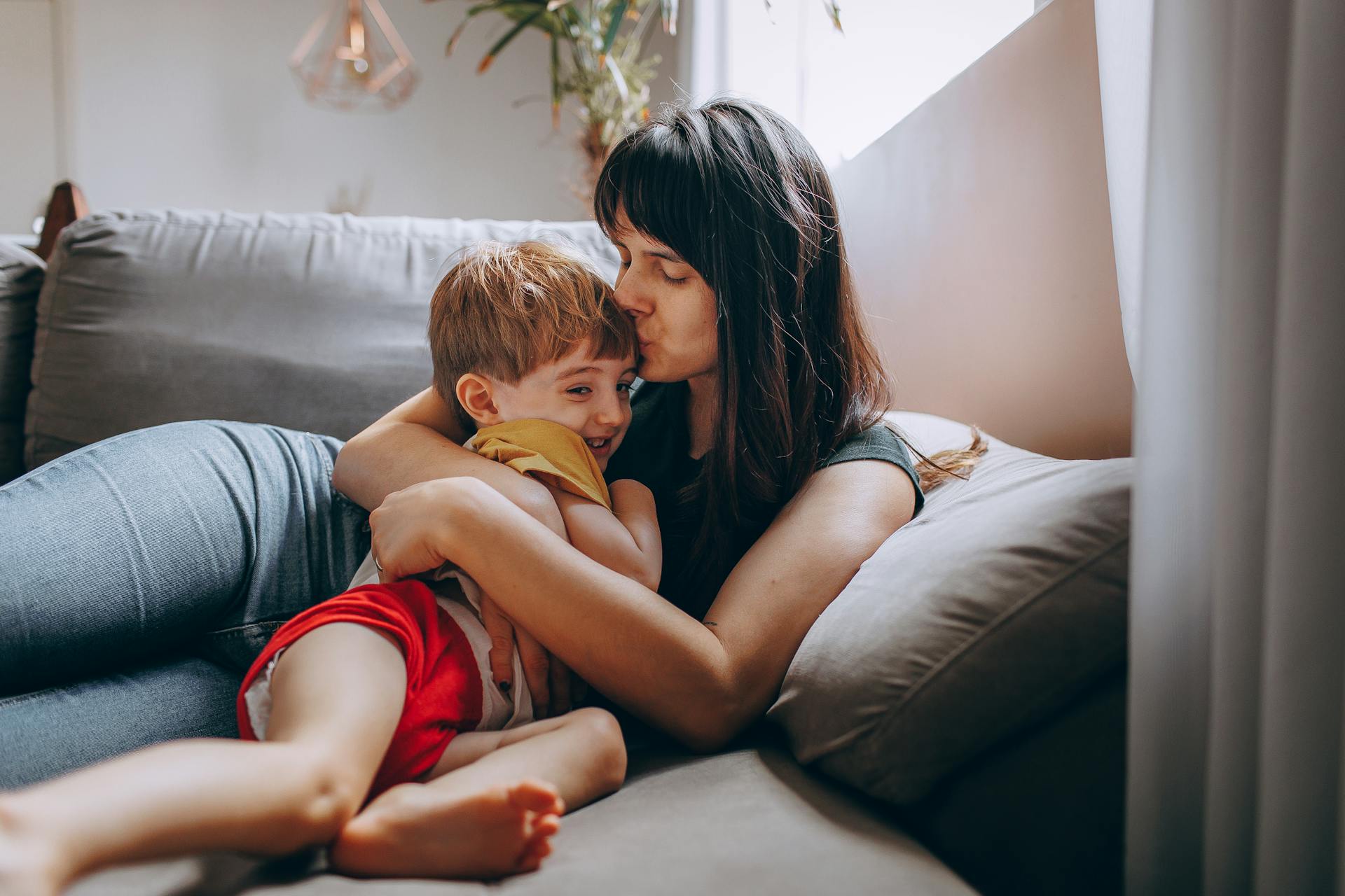 Une femme embrassant et serrant son fils dans ses bras alors qu'elle est assise sur un canapé | Source : Pexels