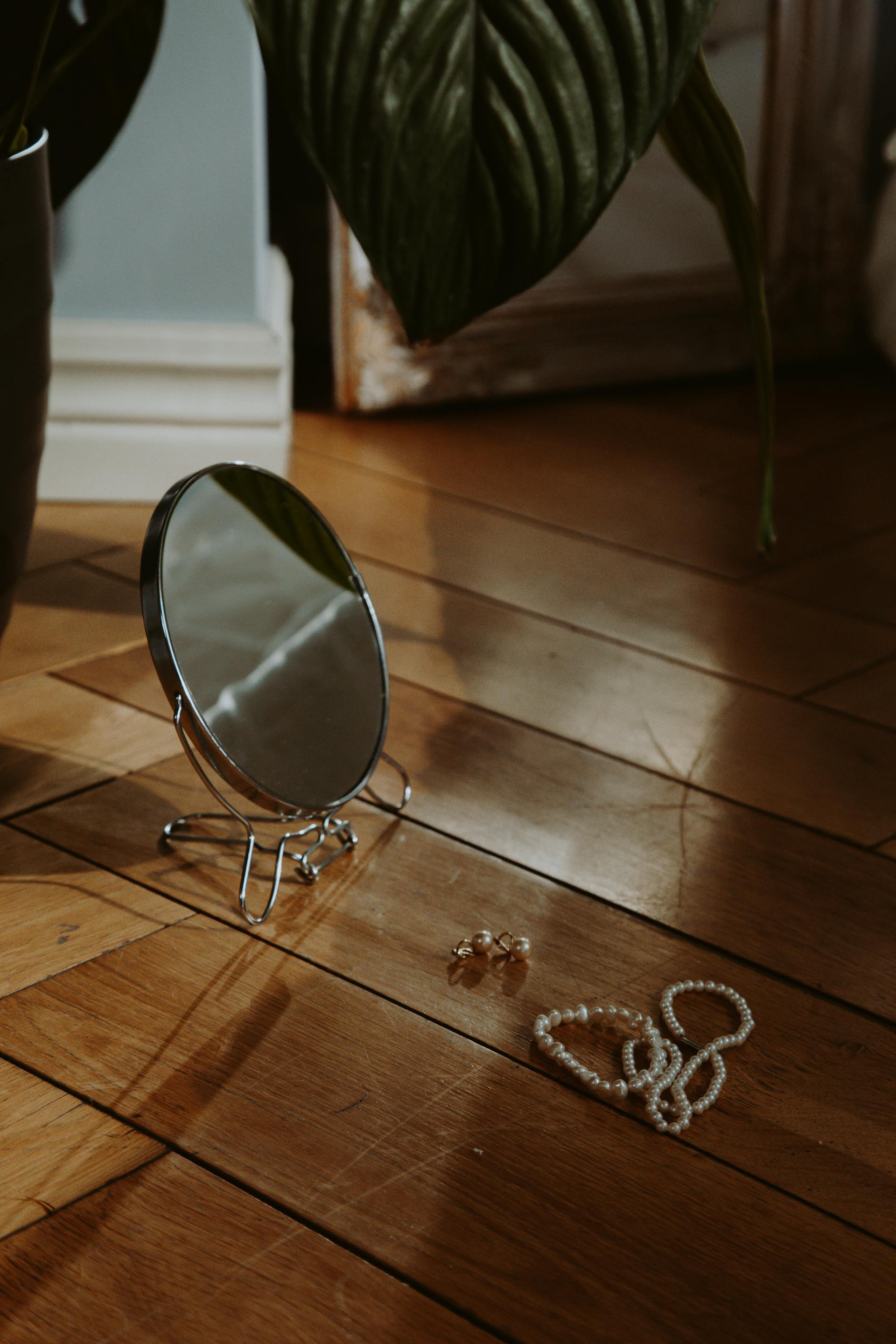 Un miroir rond encadré d'argent et des bijoux posés sur le sol en bois | Source : Pexels