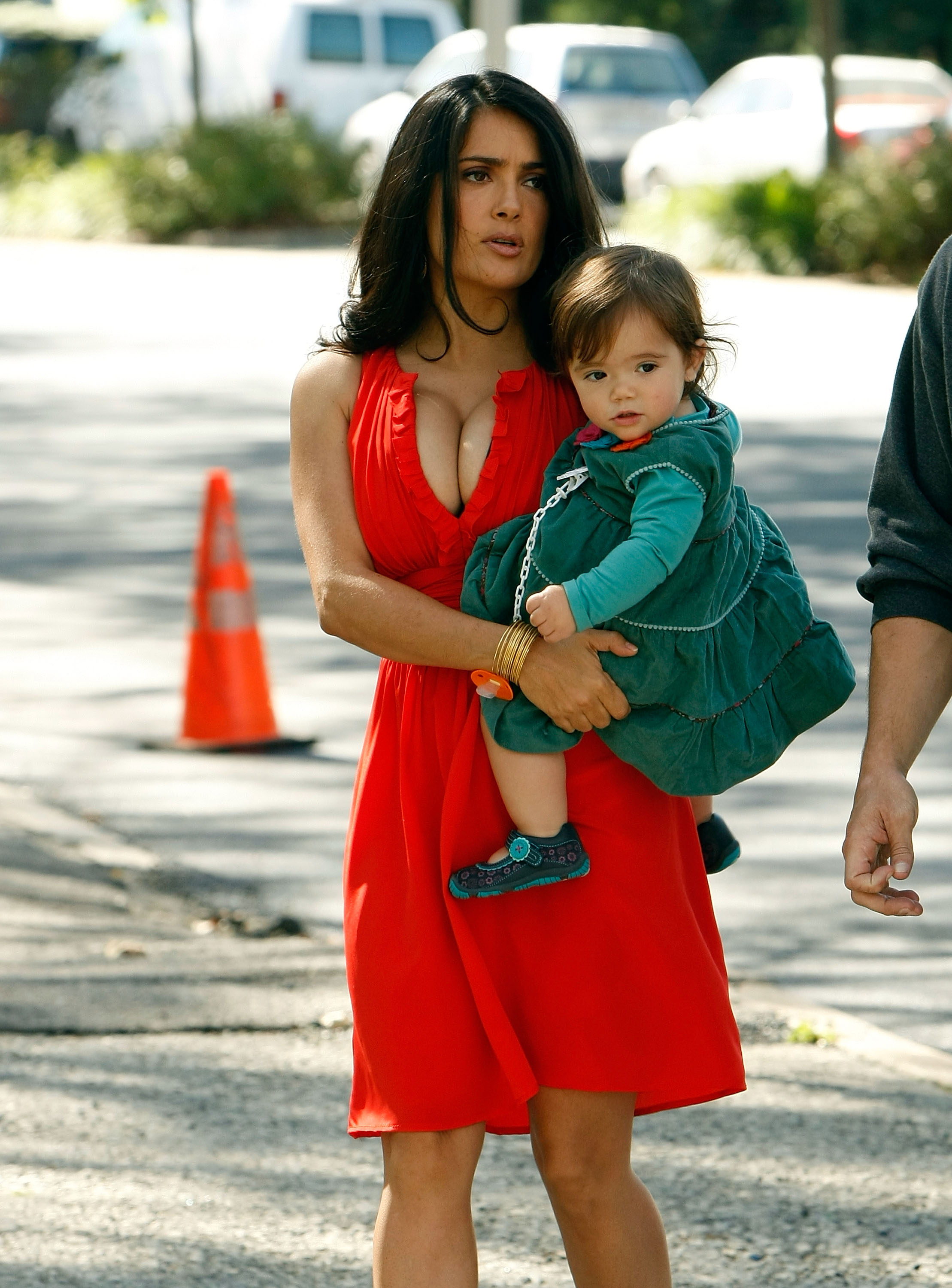 On voit Salma Hayek porter dans ses bras la petite Valentina Pinault sur le tournage de « 30 Rock » à New York. Vêtue d'une robe rouge vif et d'accessoires dorés, Salma marche d'un pas vif sur le trottoir, l'air sérieux. Valentina, vêtue d'une robe à volants vert émeraude assortie à des leggings et des ballerines, regarde calmement au loin.