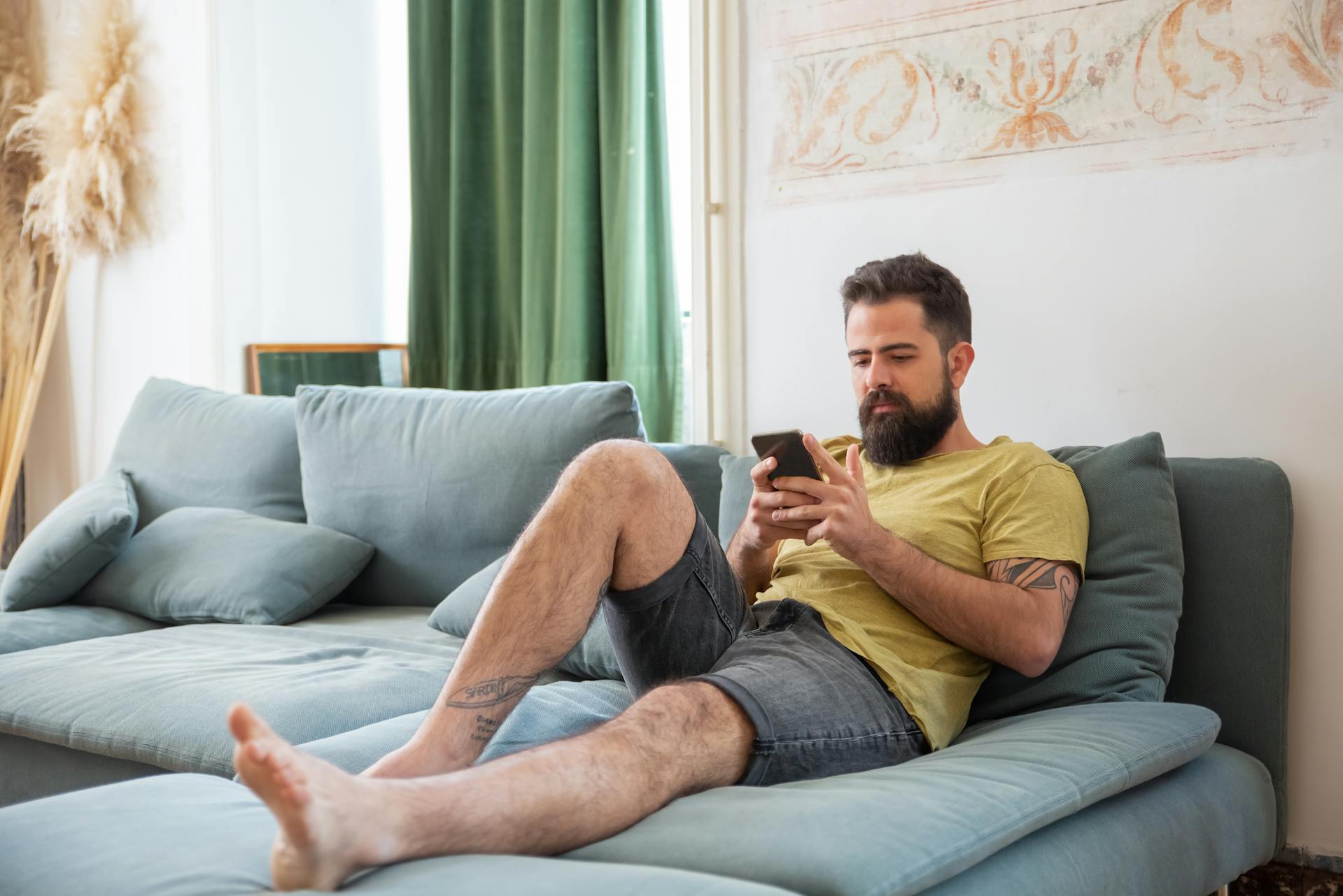 Un homme assis sur un canapé et regardant son téléphone | Source : Pexels