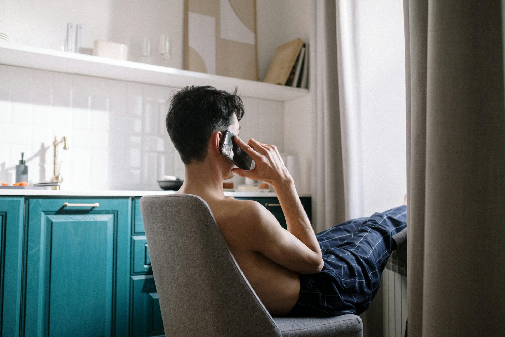 Vue latérale d'un homme assis sur une chaise et parlant au téléphone | Source : Pexels