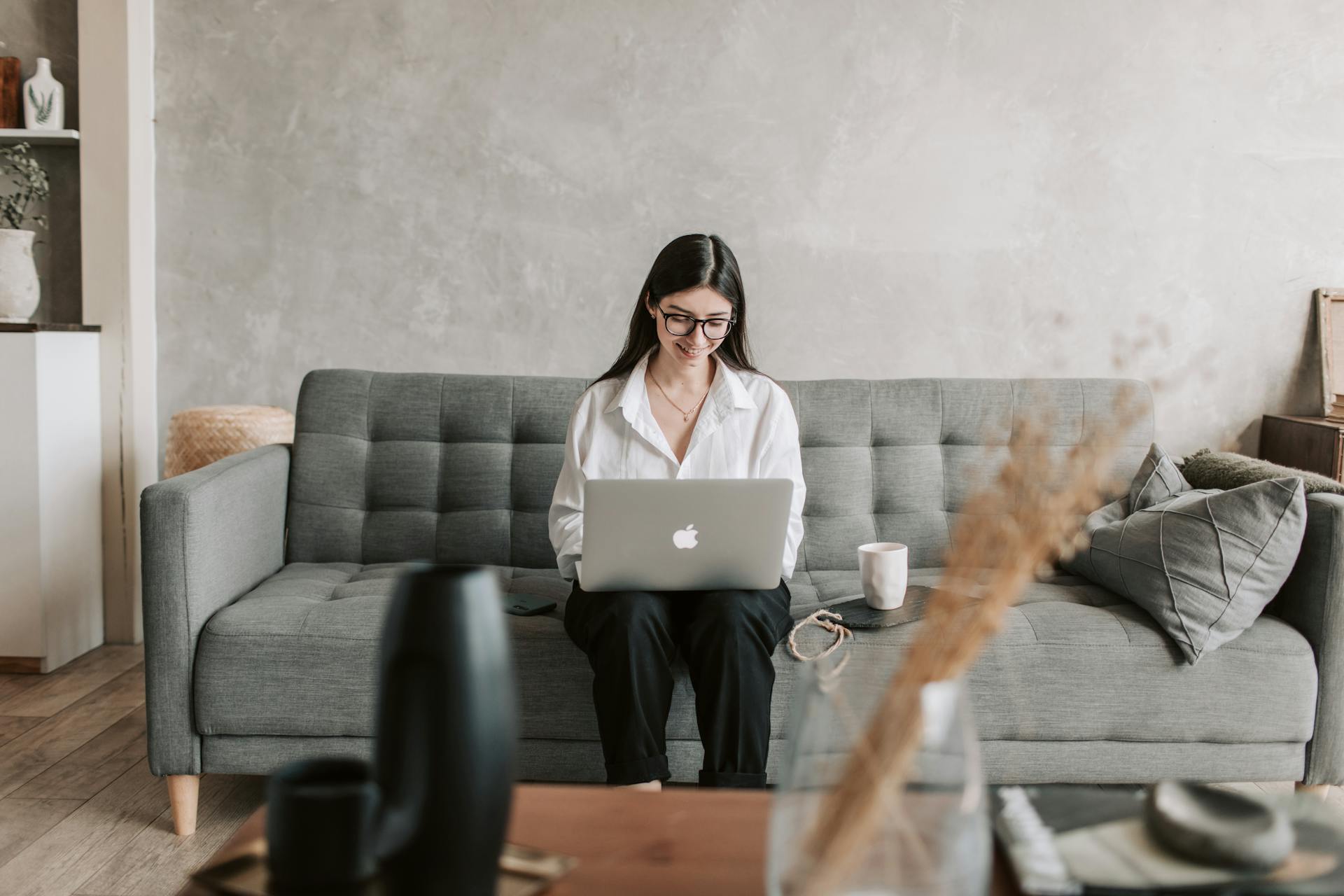 Une femme assise sur un canapé, buvant un café et utilisant un ordinateur portable | Source : Pexels