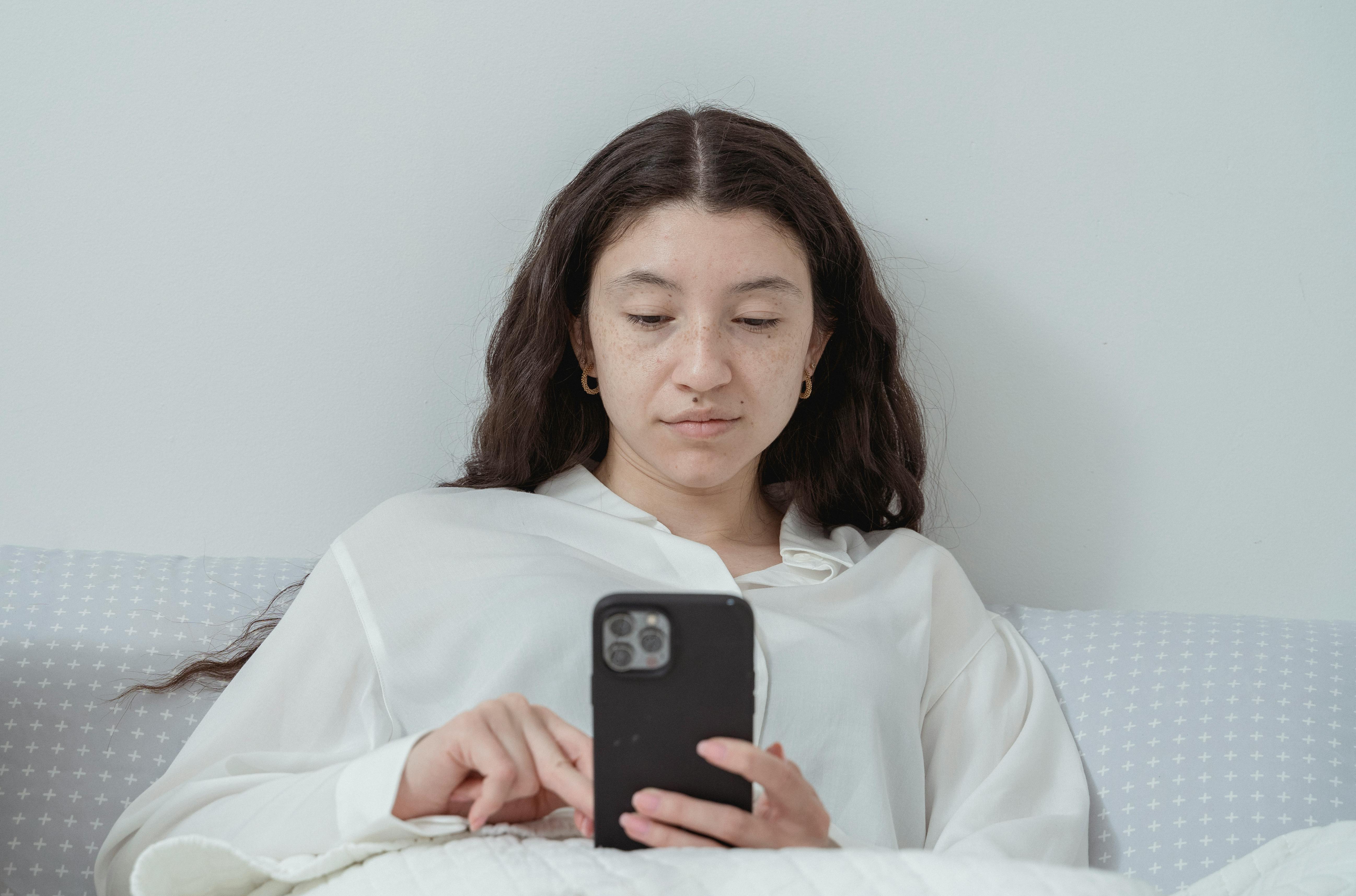 Une femme sérieuse utilisant son téléphone alors qu'elle est allongée dans son lit | Source : Pexels
