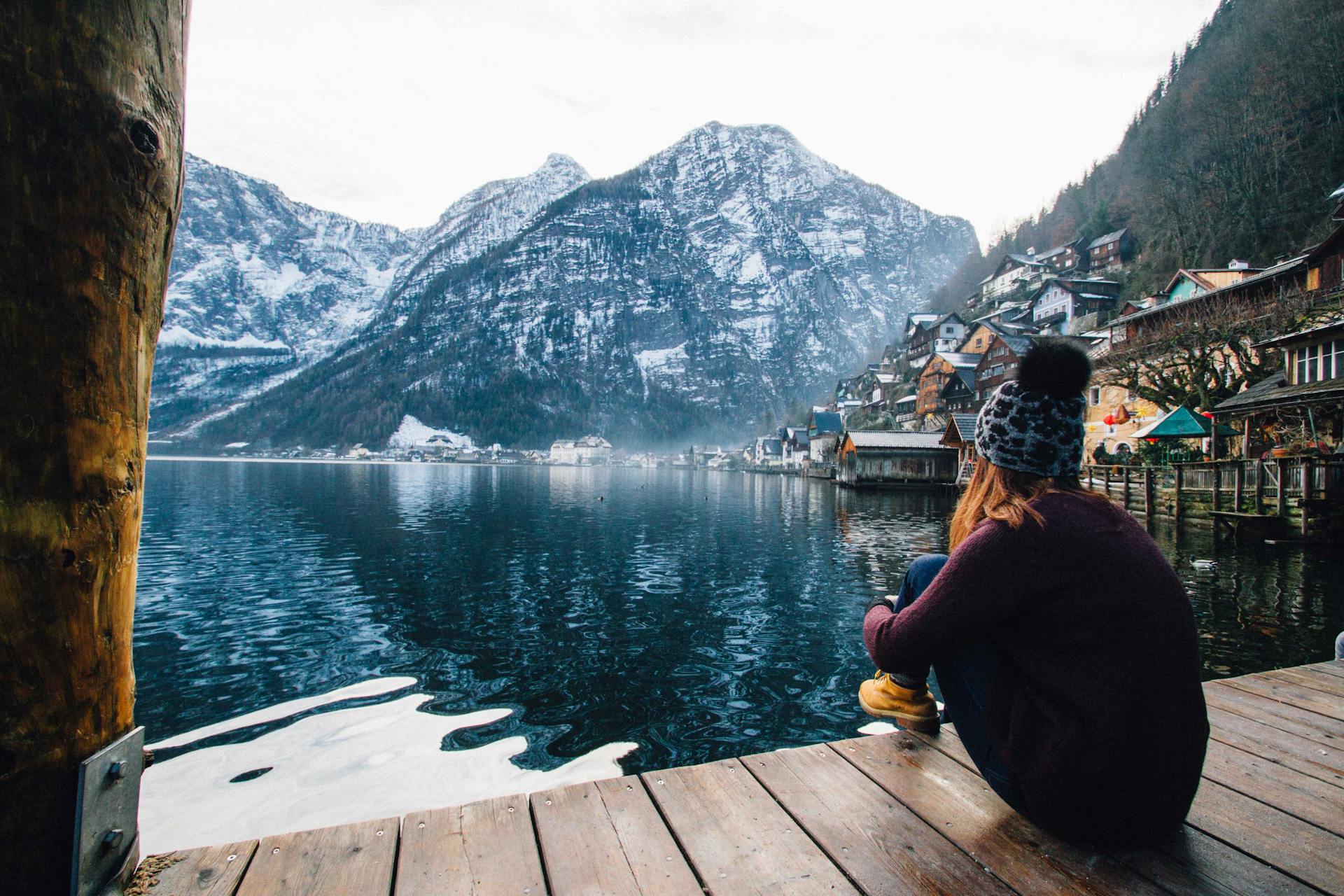 Une femme assise sur une terrasse en bois, contemplant le lac et les montagnes | Source : Pexels