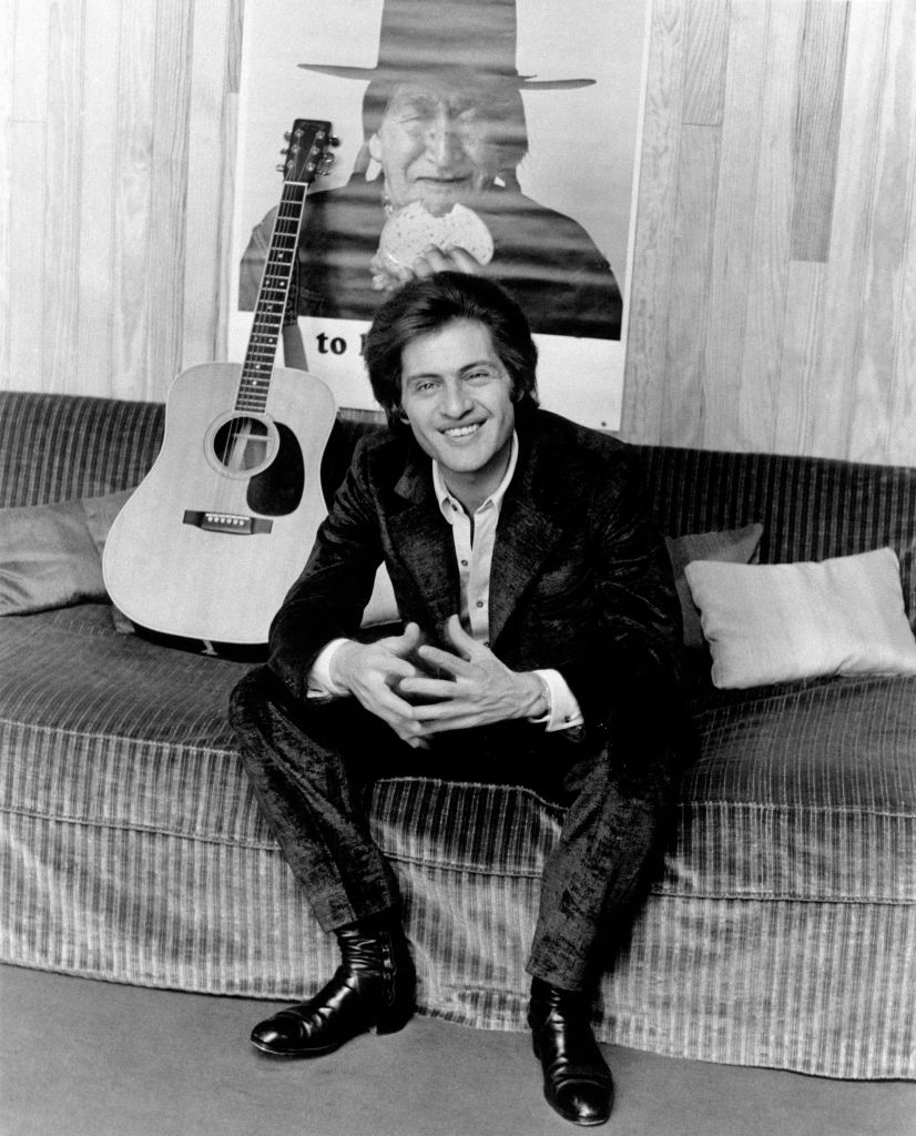 Le chanteur français d'origine américaine Joe Dassin sourit sur un canapé à côté d'une guitare. Paris, années 1970 I Source : Getty Images