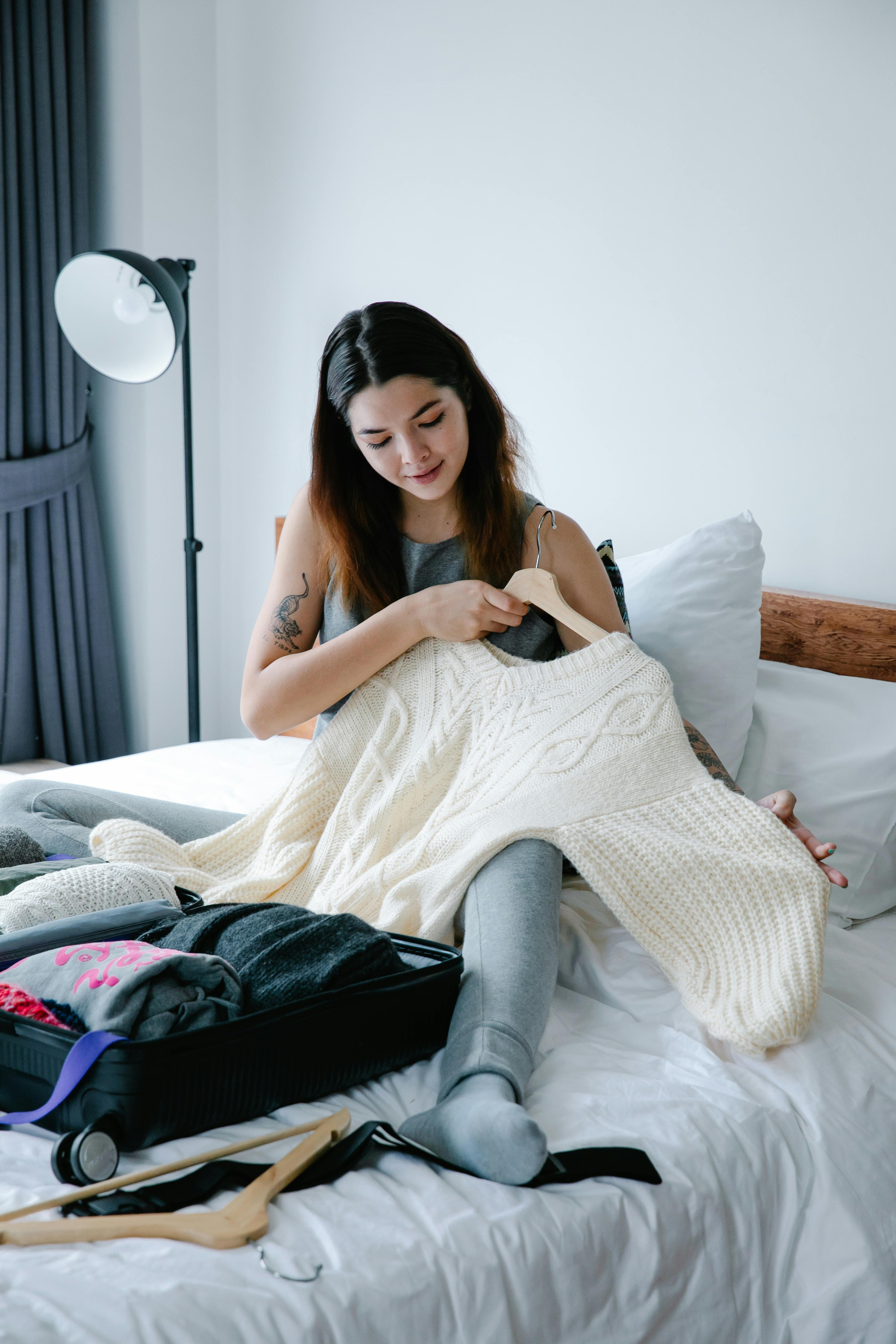 Une femme assise sur le lit tout en tenant un pull | Source : Pexels