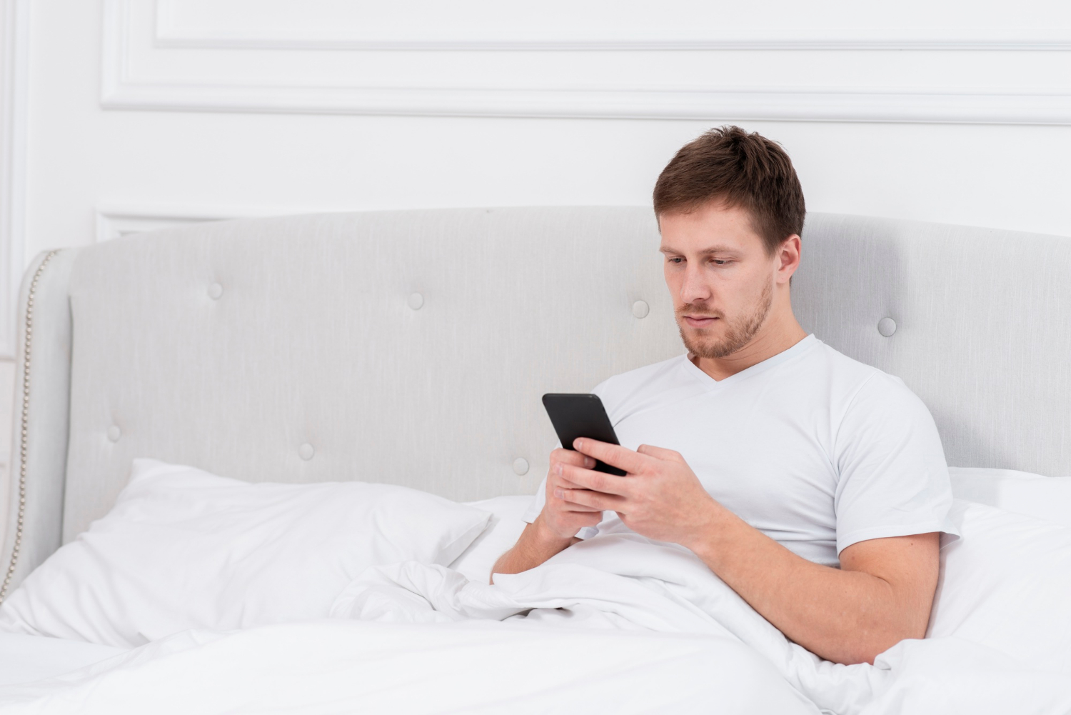 Un homme assis sur son lit et fixant son téléphone | Source : Freepik