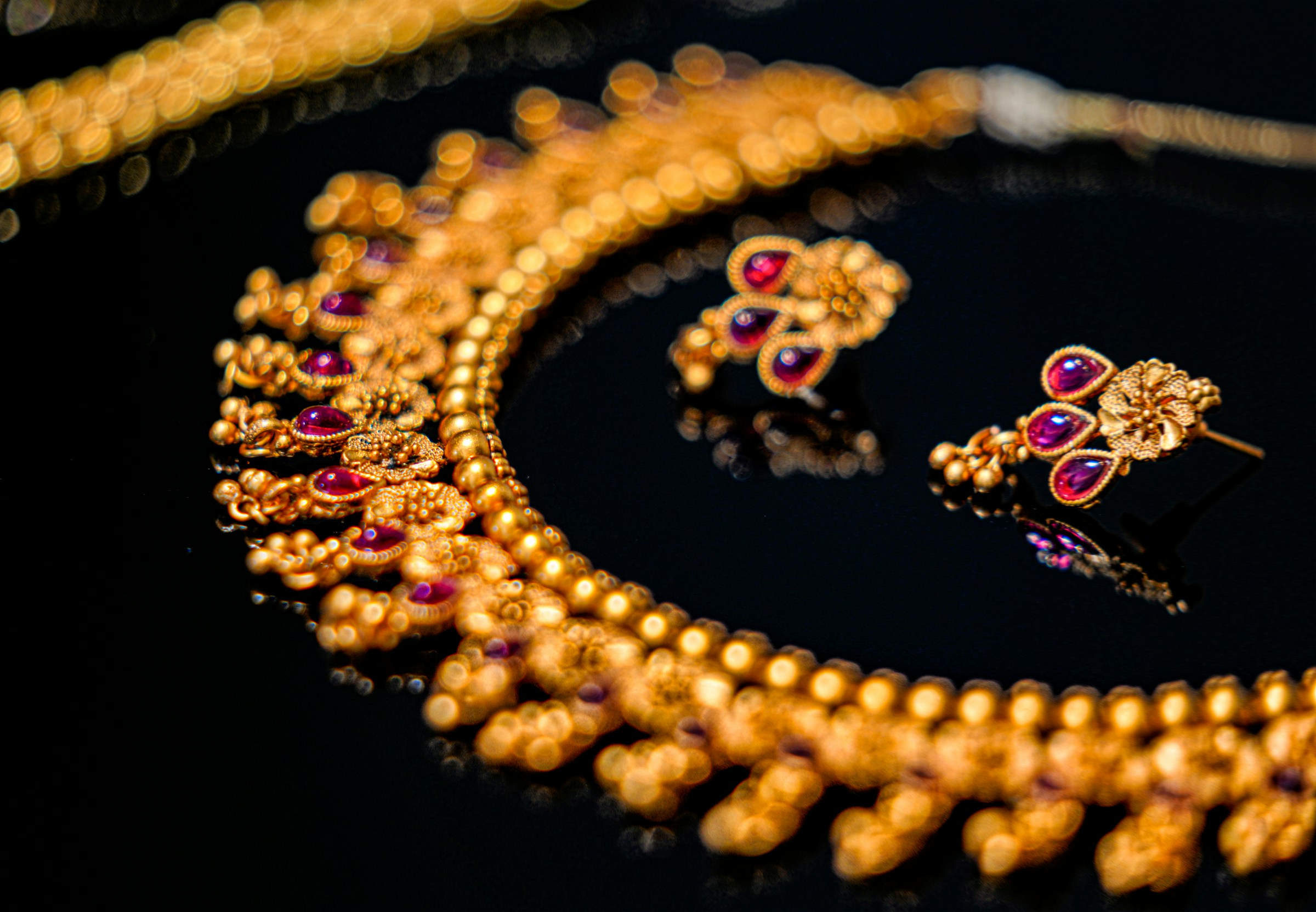 Un collier doré avec des boucles d'oreilles décorées de pierres précieuses rouges et violettes | Source : Unsplash
