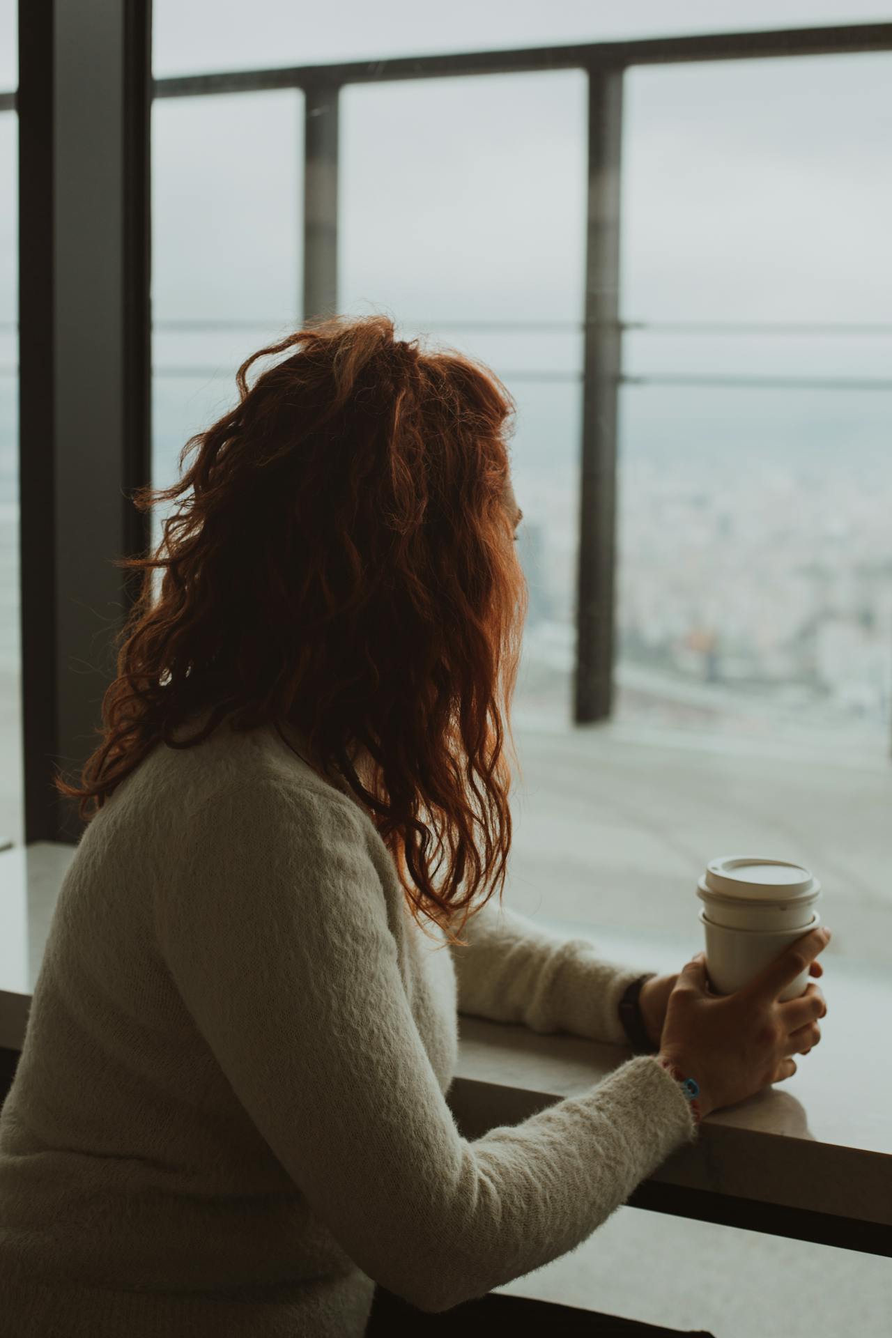 Une femme assise avec une tasse de café devant une fenêtre en verre | Source : Pexels