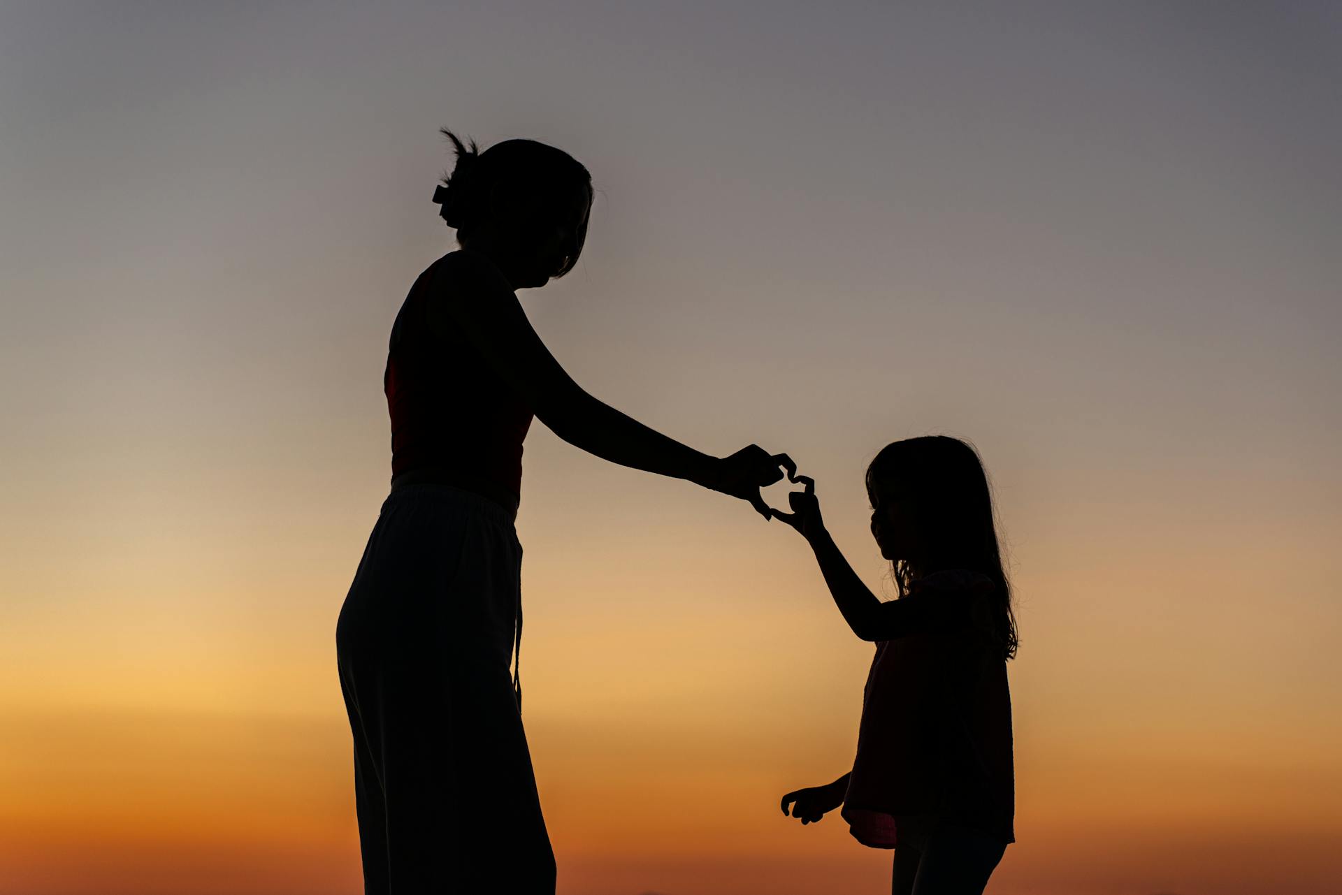 Silhouette d'une mère et de sa fille faisant le geste de la main et du cœur | Source : Pexels