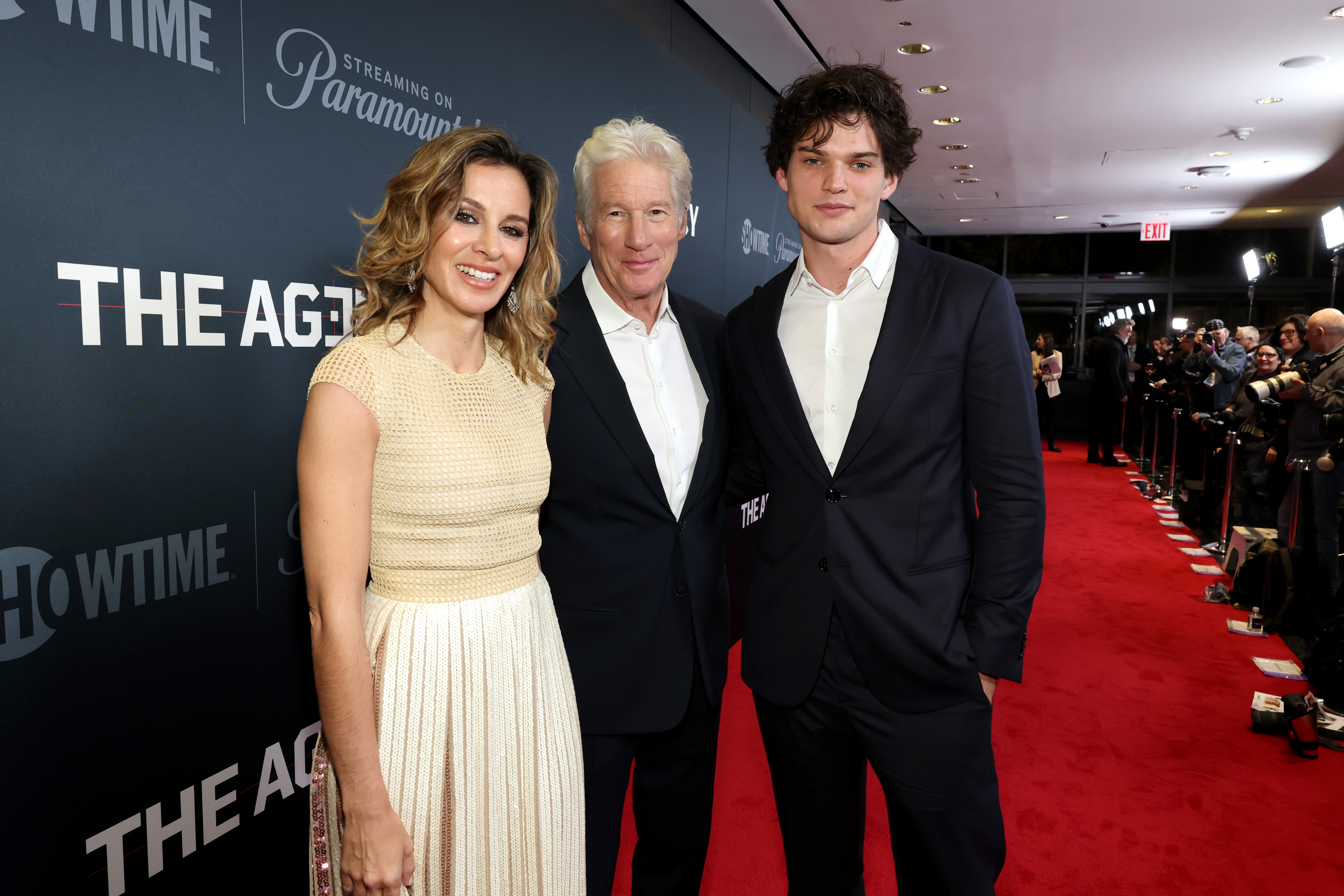 Tout sourire et sophistication, Homer Gere se tient entre Alejandra et Richard Gere lors de la première de The Agency. Les flashs crépitent alors que le trio illumine le tapis rouge à New York.