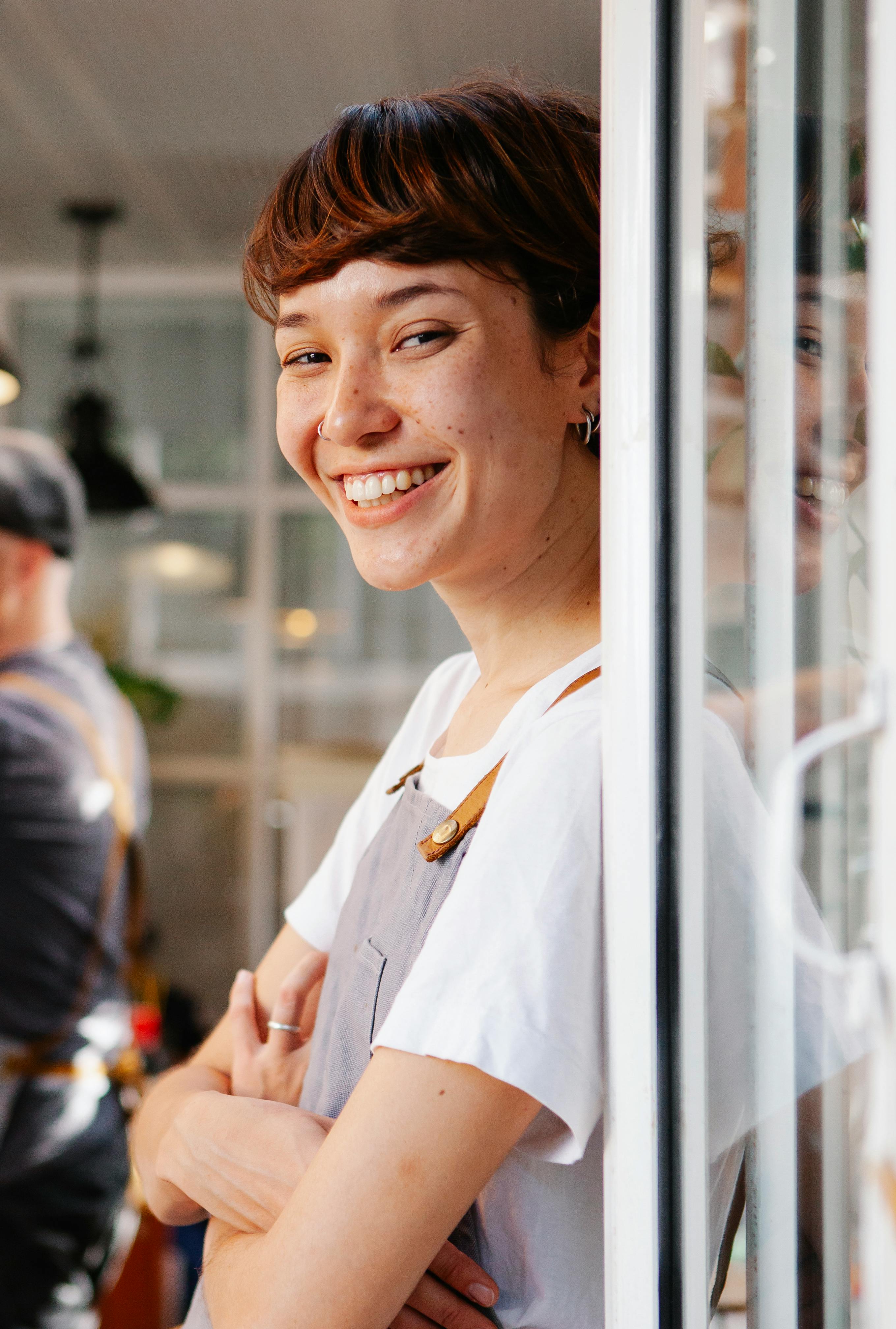 Une serveuse heureuse se tenant à la porte d'un restaurant | Source : Pexels
