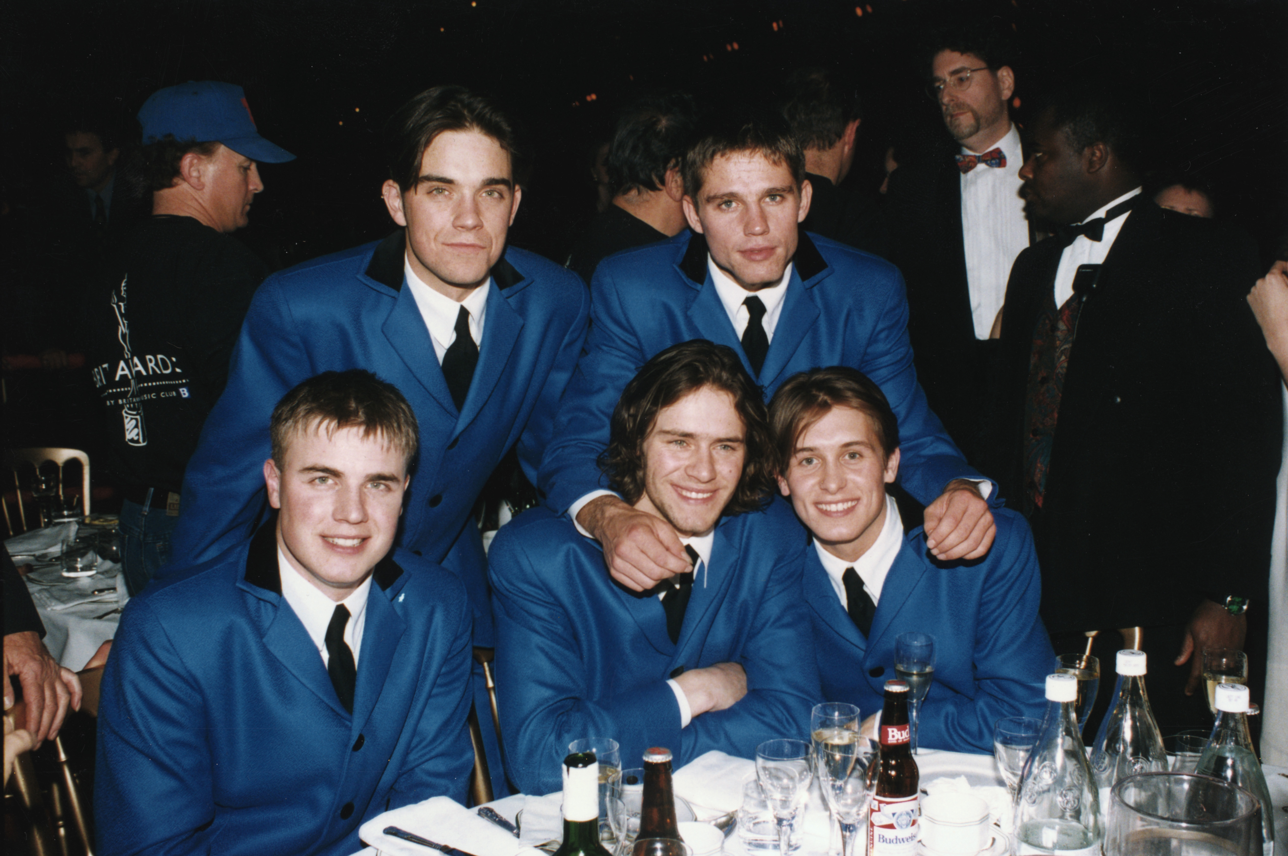 Robbie Williams et ses camarades du groupe Take That assistent aux Brit Awards en 1994, vêtus de costumes bleu électrique assortis. Au sommet de leur gloire, le groupe dominait les charts britanniques, et leur look soigné reflétait parfaitement leur statut de géants de la pop.