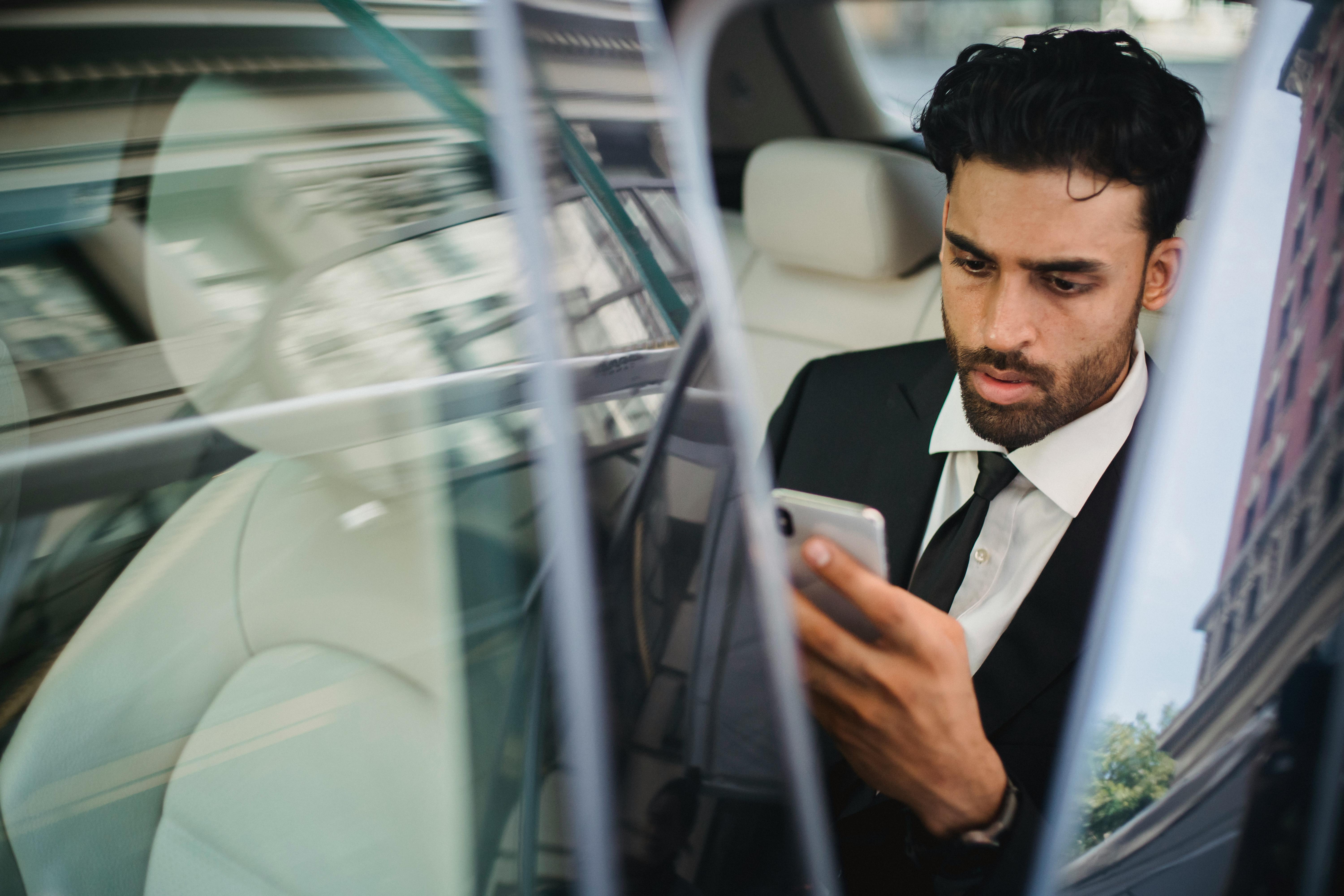 Un homme sérieux qui regarde son téléphone alors qu'il est assis dans une voiture | Source : Pexels
