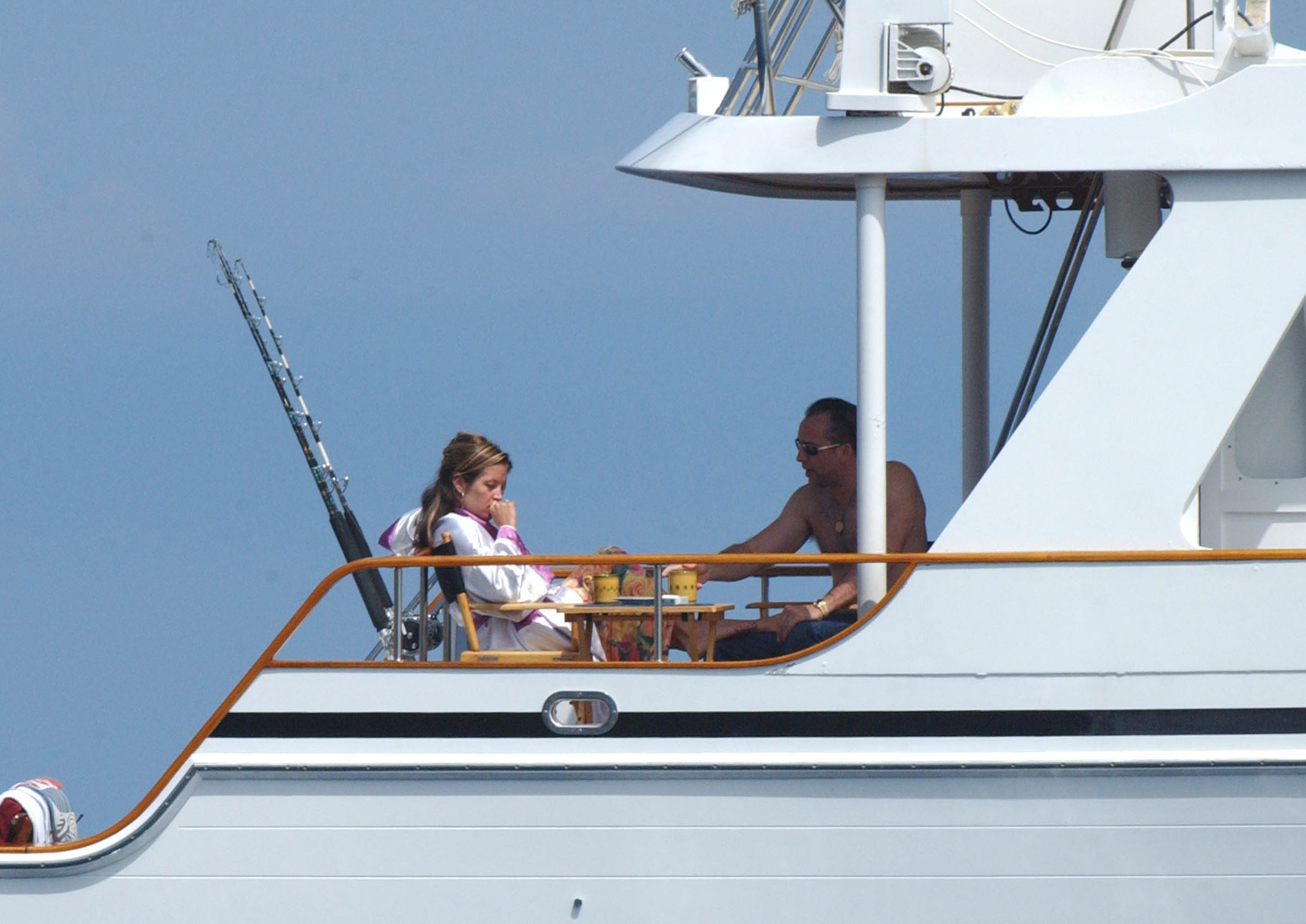 Lisa Marie Presley et Nicolas Cage aperçus à bord d'un yacht près de l'île Catalina le 4 septembre 2001. Presley était assise dans une chaise longue, vêtue d'un peignoir blanc, l'air calme et pensif, tandis que Cage, torse nu et portant des lunettes de soleil, se penchait vers elle par-dessus une petite table.