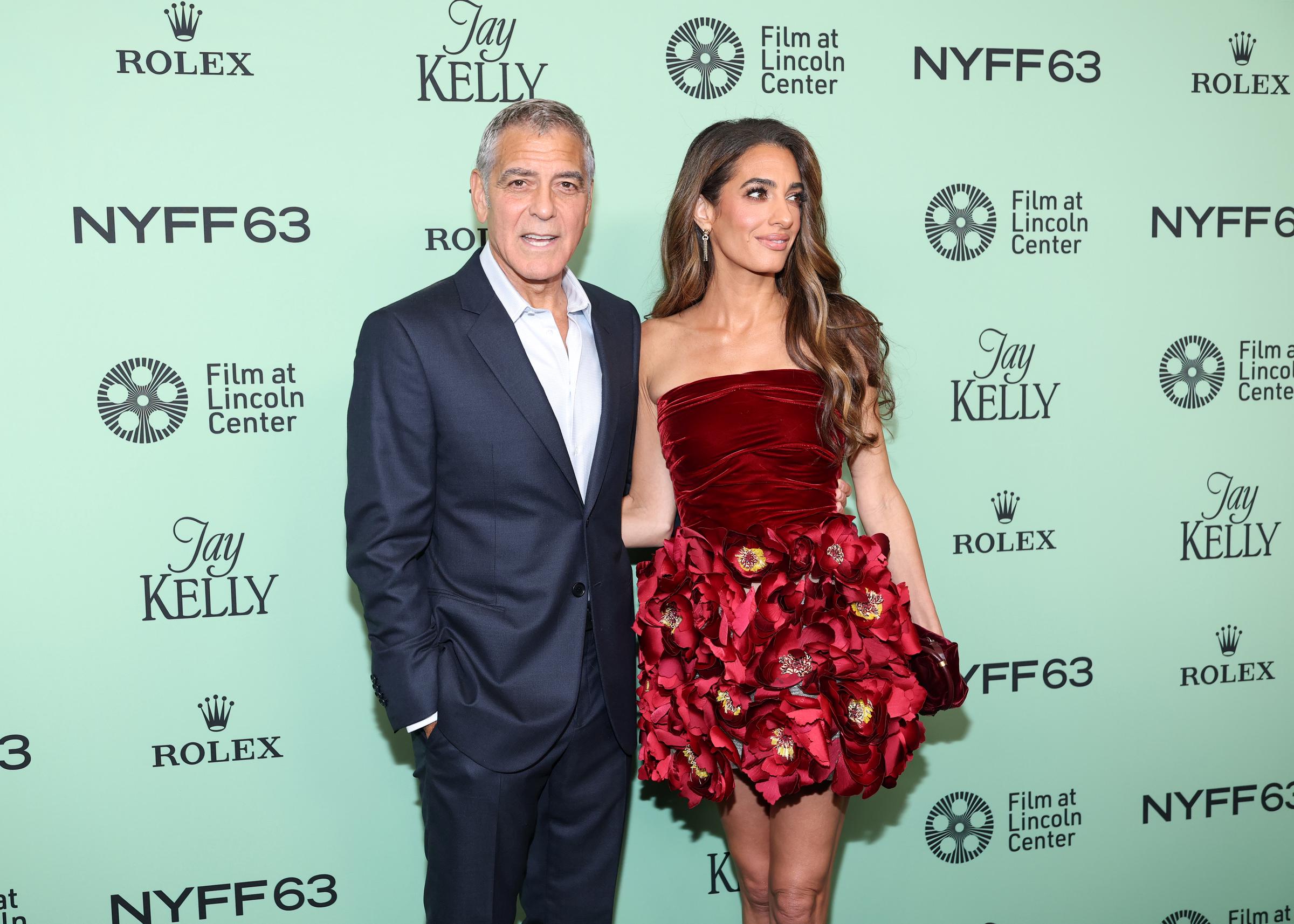 Dans un plan large avec le festival en toile de fond, George Clooney et Amal Clooney posent avec assurance, leur complicité sur le tapis rouge parfaitement capturée dans un cadrage équilibré.