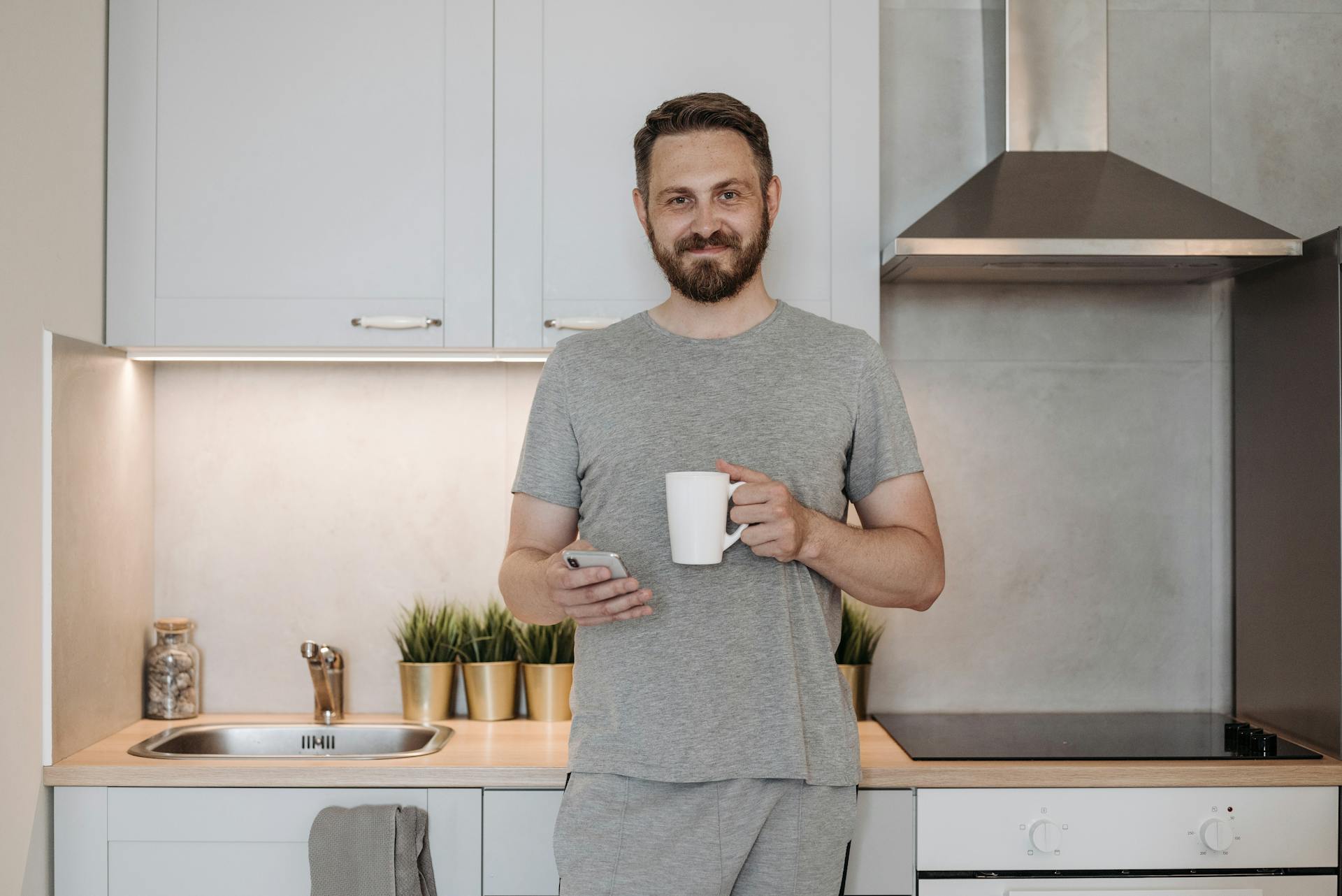 Un homme tenant un téléphone et une tasse tout en se tenant dans la cuisine | Source : Pexels