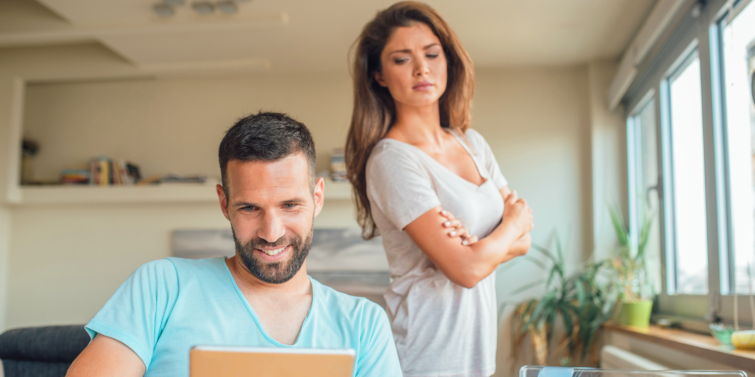 Une femme se tenant derrière un homme travaillant sur son ordinateur portable | Source : Getty Images