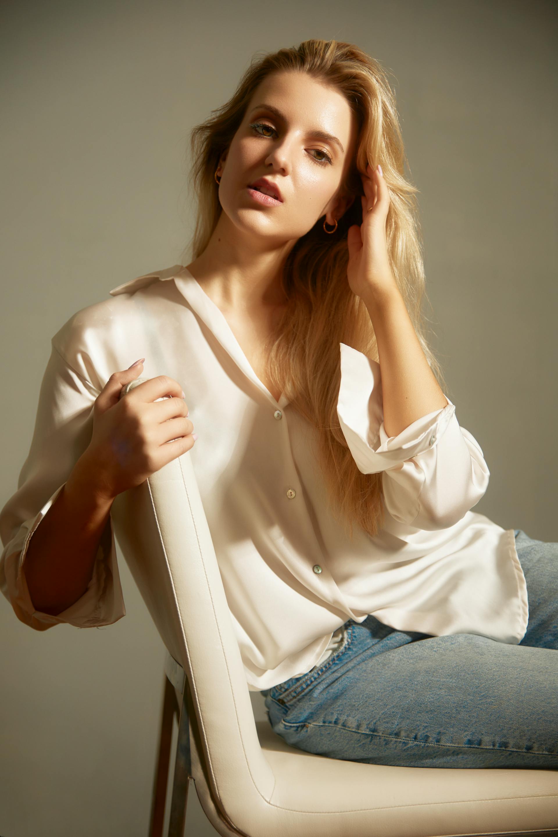 Une femme blonde vêtue d'une chemise en soie blanche et d'un jean, assise sur une chaise blanche | Source : Pexels