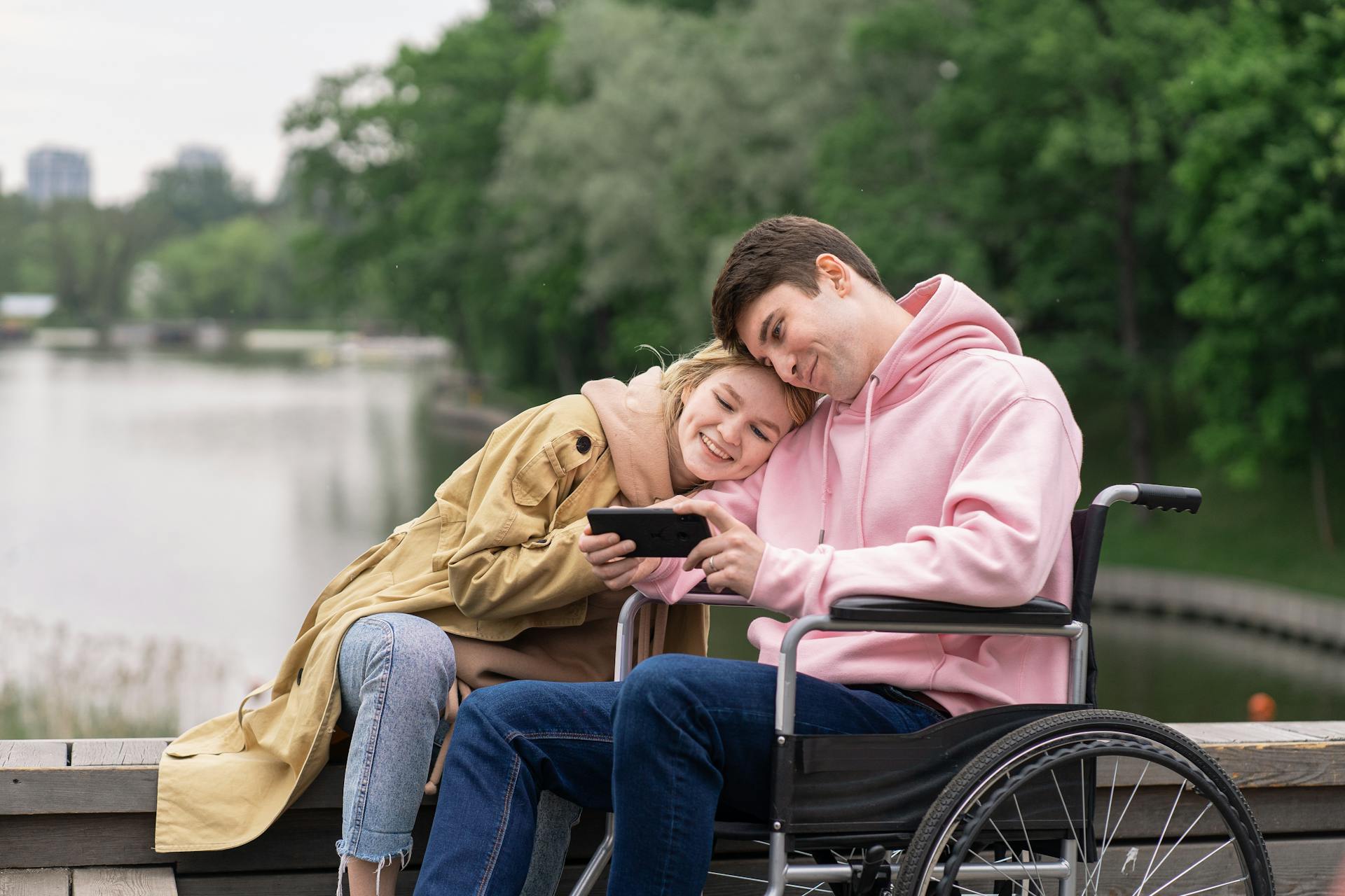 Un homme en fauteuil roulant regardant un smartphone à côté de sa femme | Source : Pexels