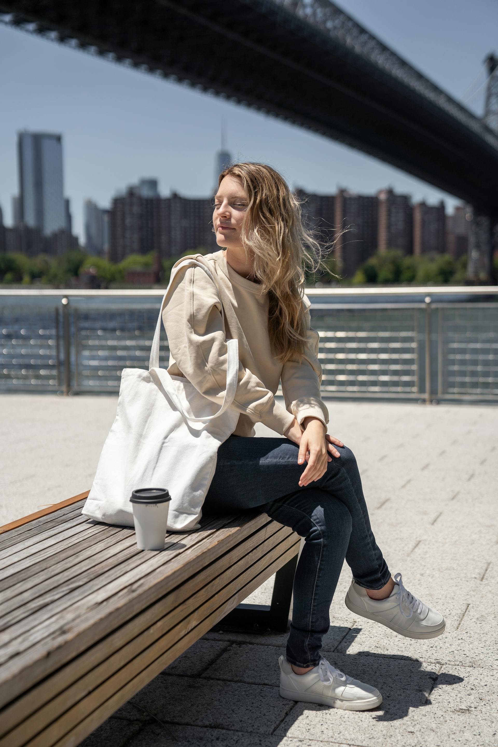 Une femme assise sur un banc avec son sac blanc et un café | Source : Pexels