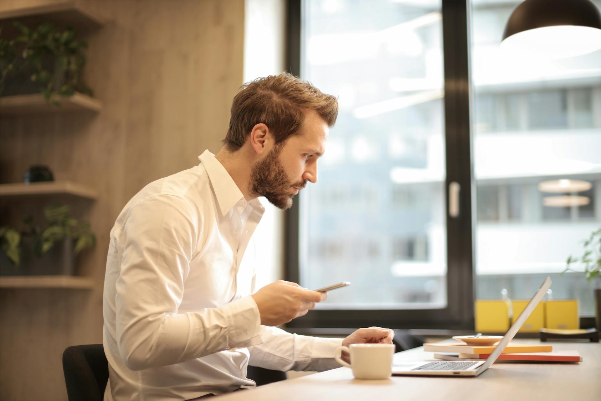 Un homme travaillant à son bureau avec un ordinateur portable et un téléphone cellulaire | Source : Pexels