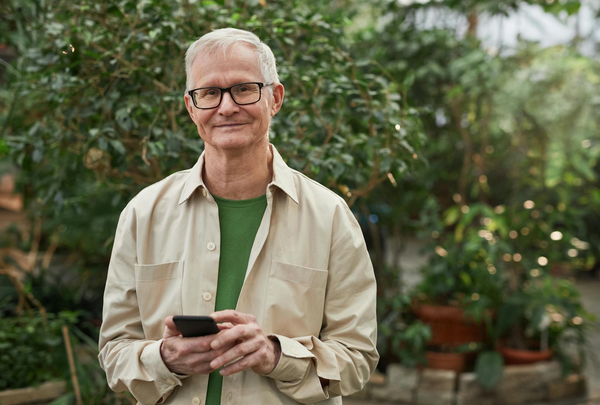 Un homme d'âge mûr heureux, avec des lunettes et une chemise à boutons, tenant un téléphone | Source : Pexels