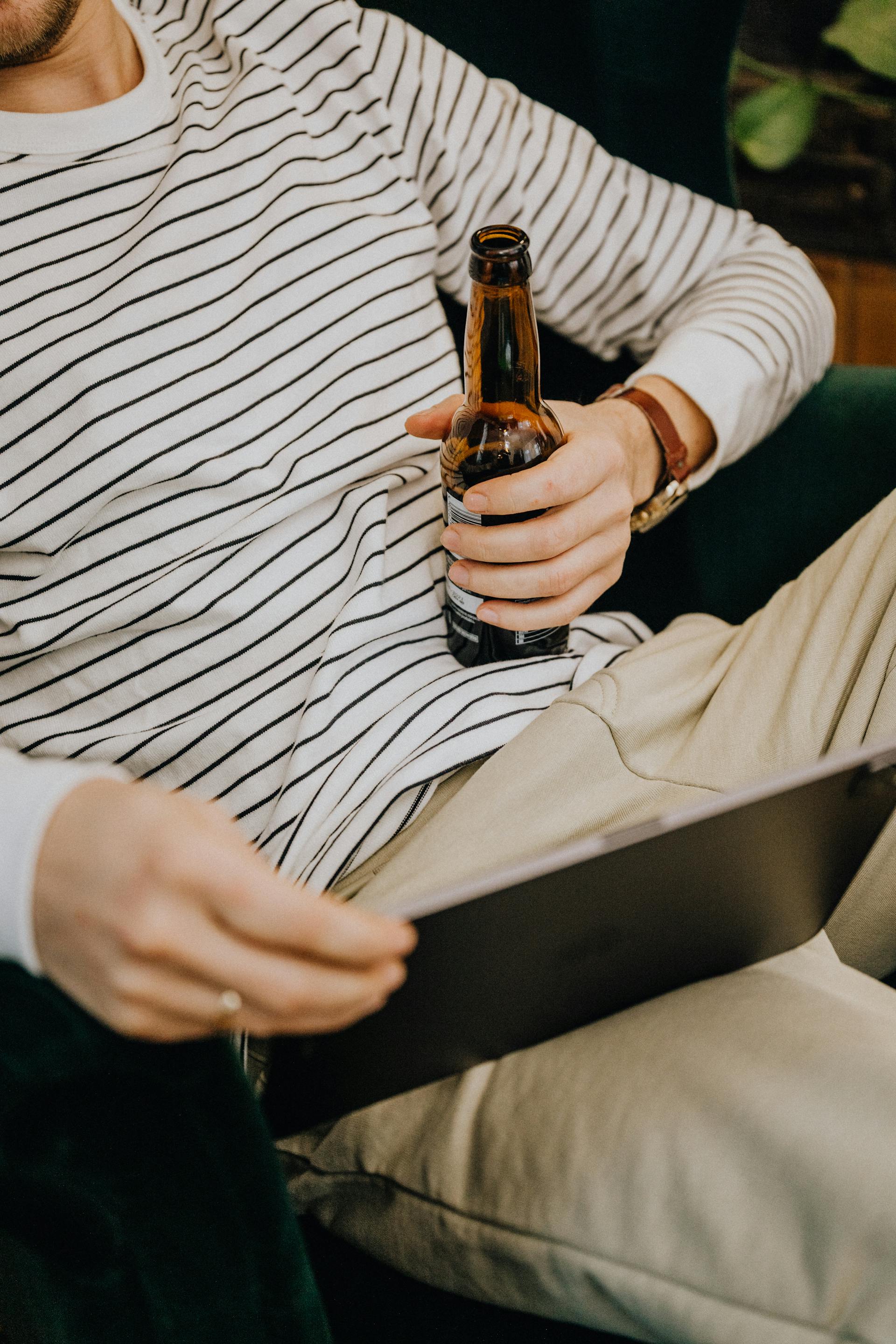 Gros plan sur un homme tenant une bouteille de bière et regardant sa tablette | Source : Pexels